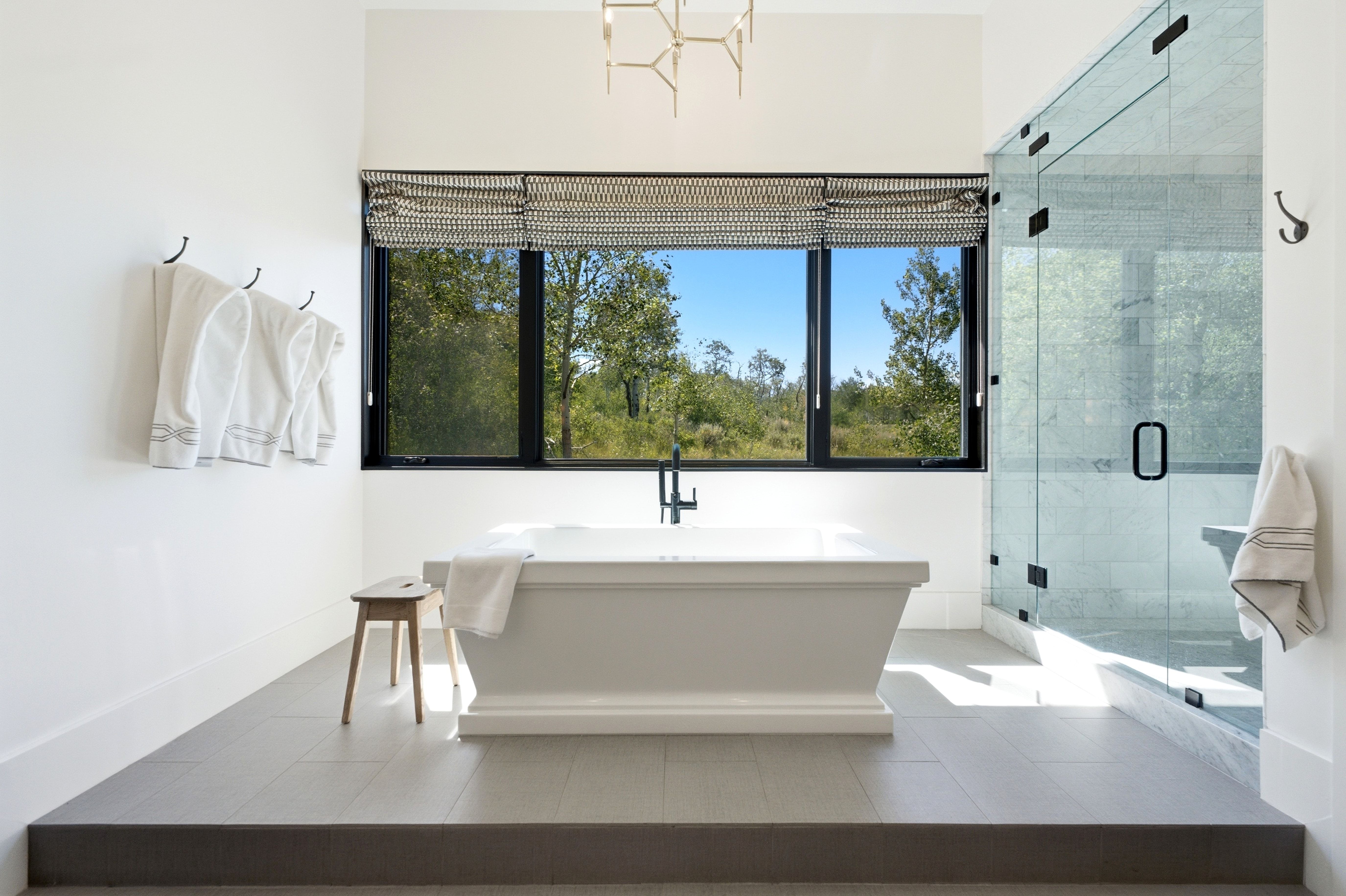 Freestanding soaking tub with a modern floor-mounted faucet, complemented by a large window with a patterned roller shade