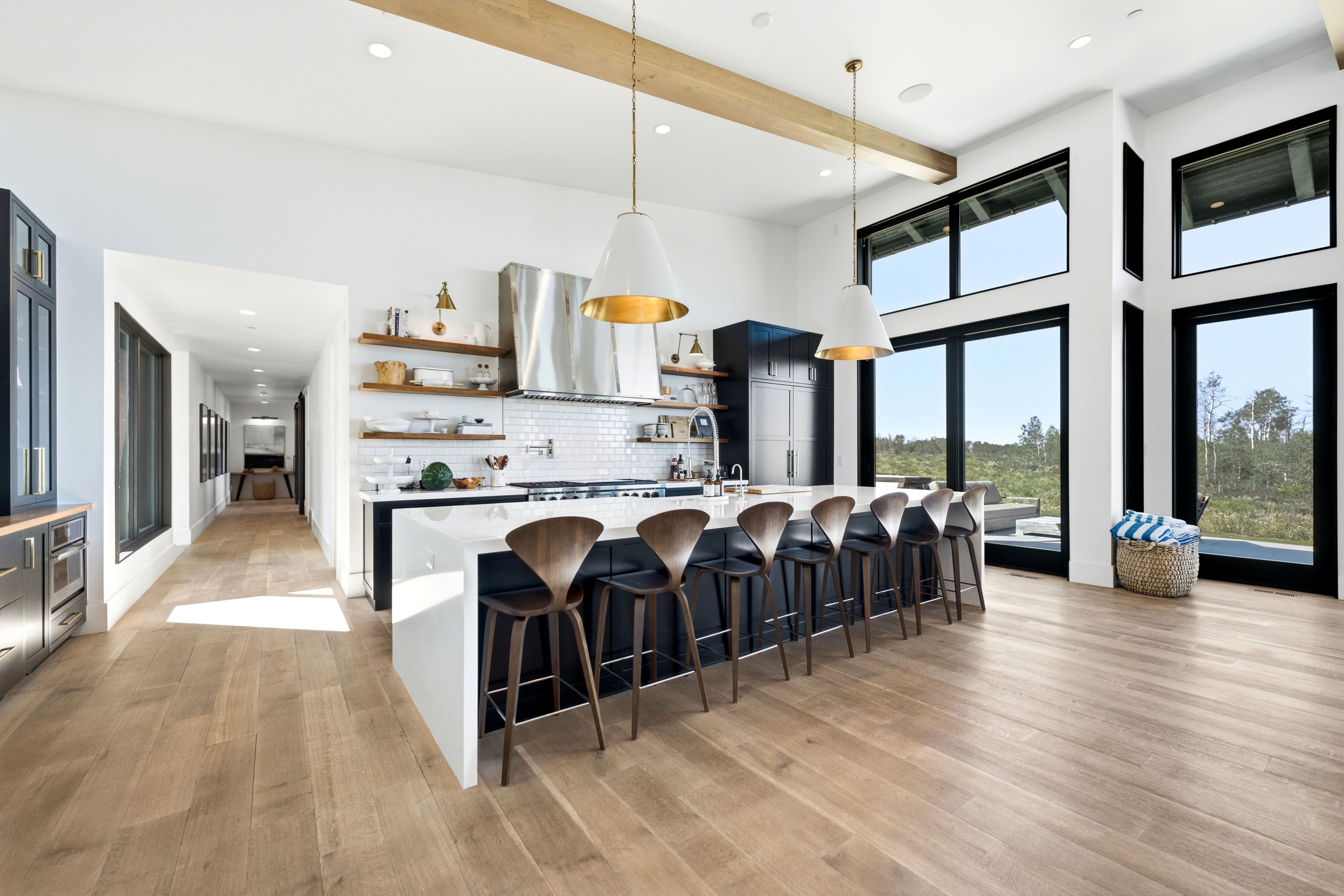 Expansive kitchen featuring an oversized island with countertop seating, a subway tile backsplash, stainless steel range hood, and open shelving