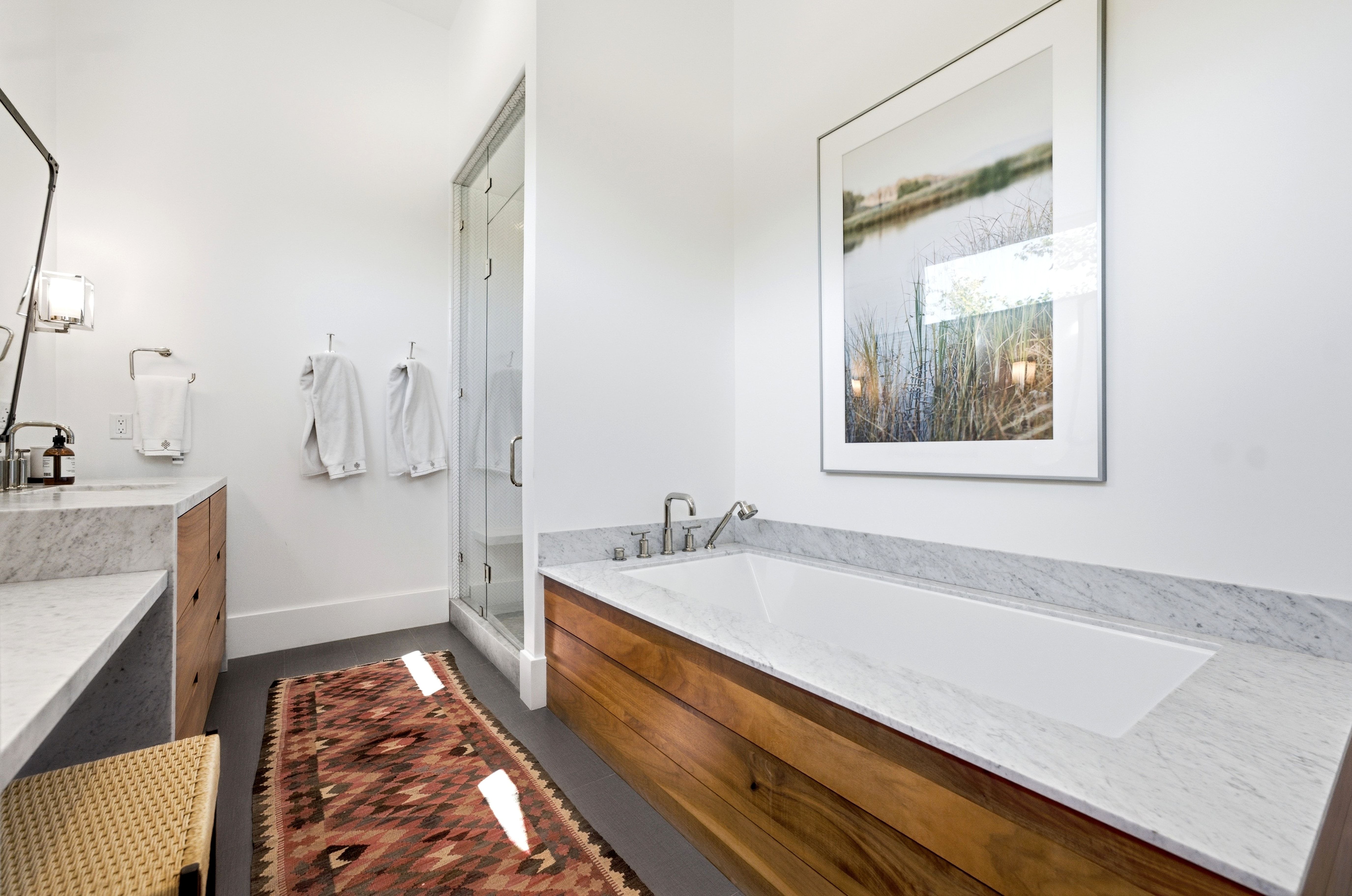 White soaking tub with surrounding marble countertop, integrated with a natural wood-finish base