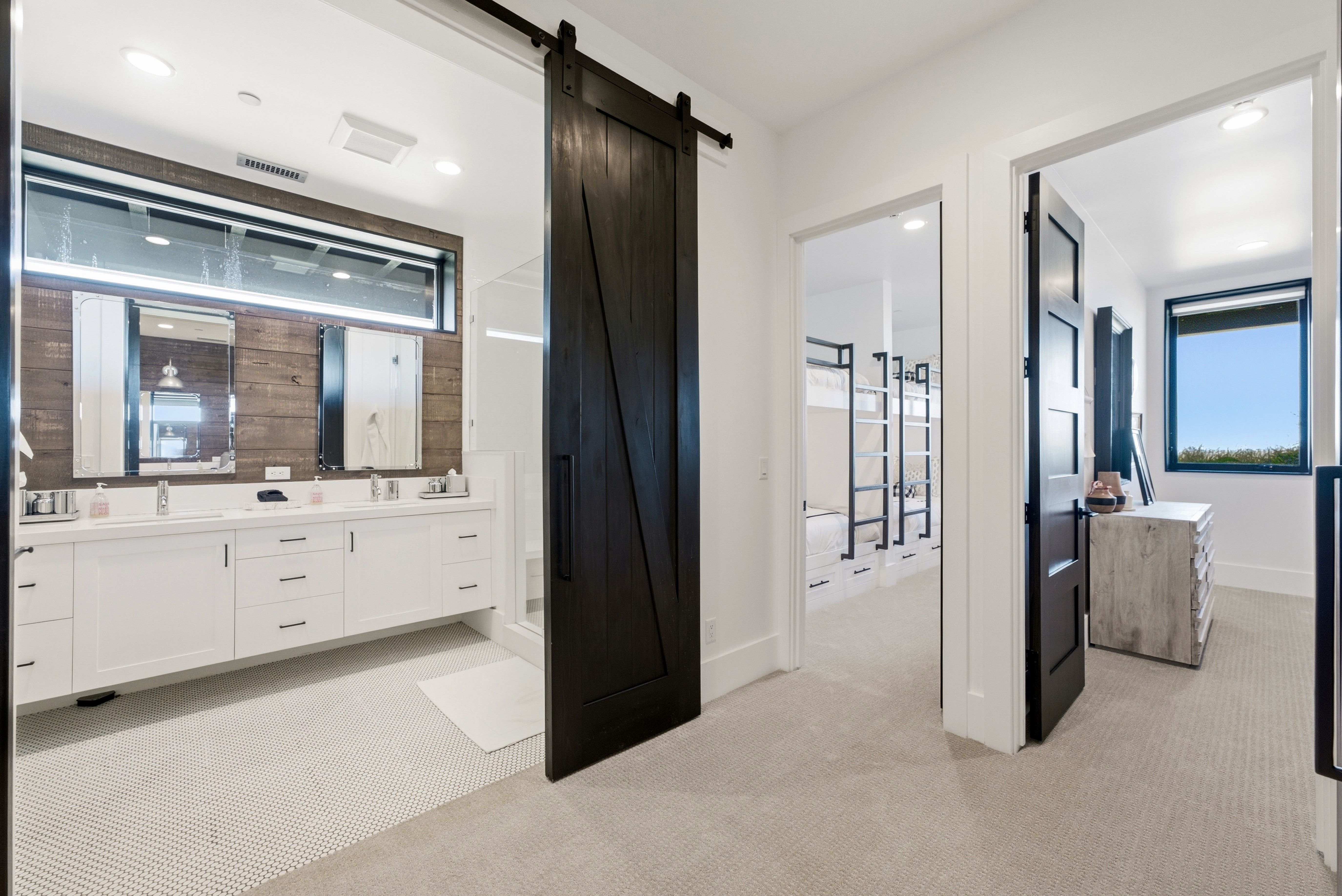 Bathroom featuring a dual vanity with white cabinetry, wood-paneled accent wall, and horizontal transom window