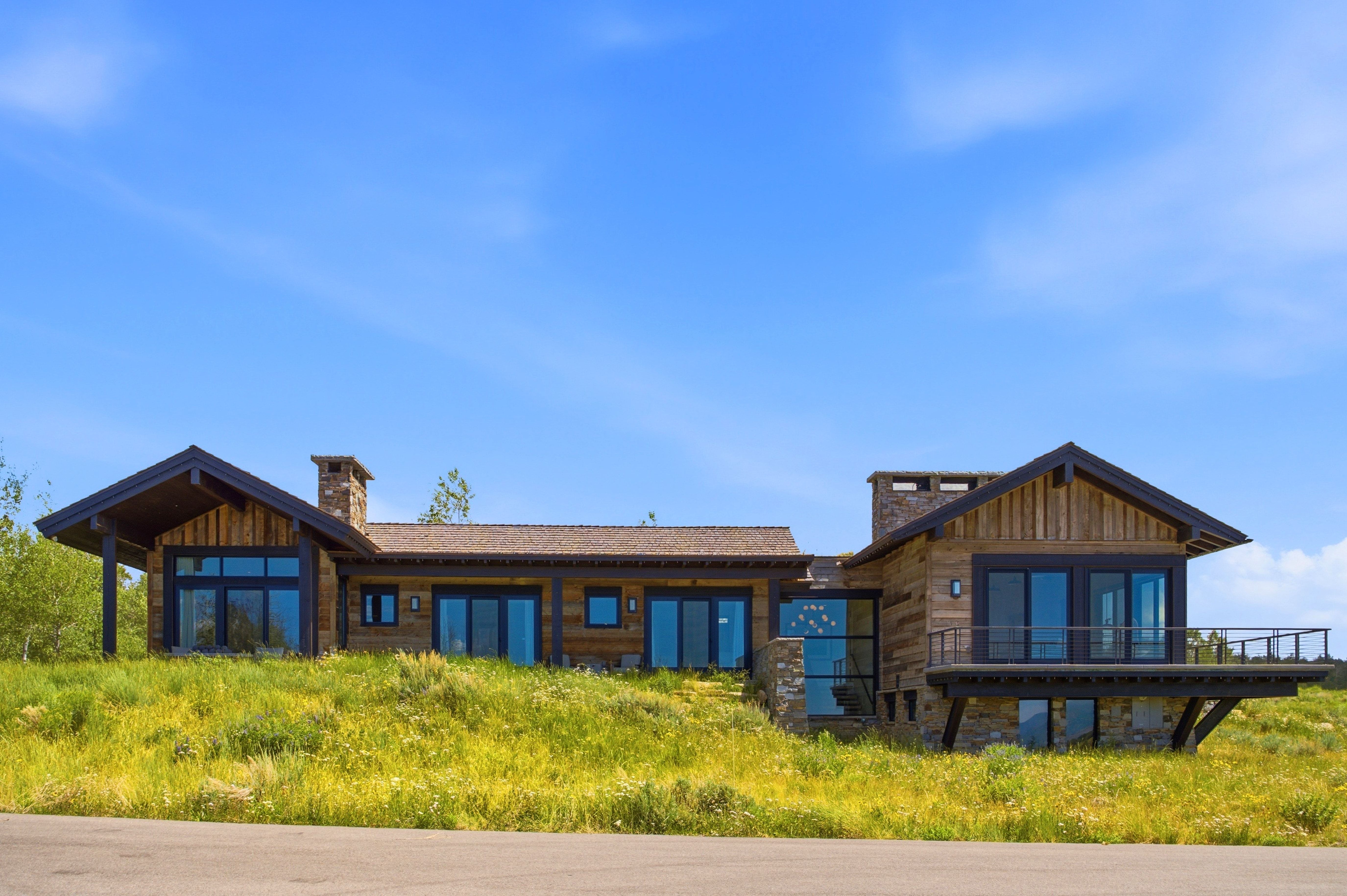 Rustic modern architecture featuring wood siding, stone accents, multiple large windows, and a cantilevered deck with dark railings
