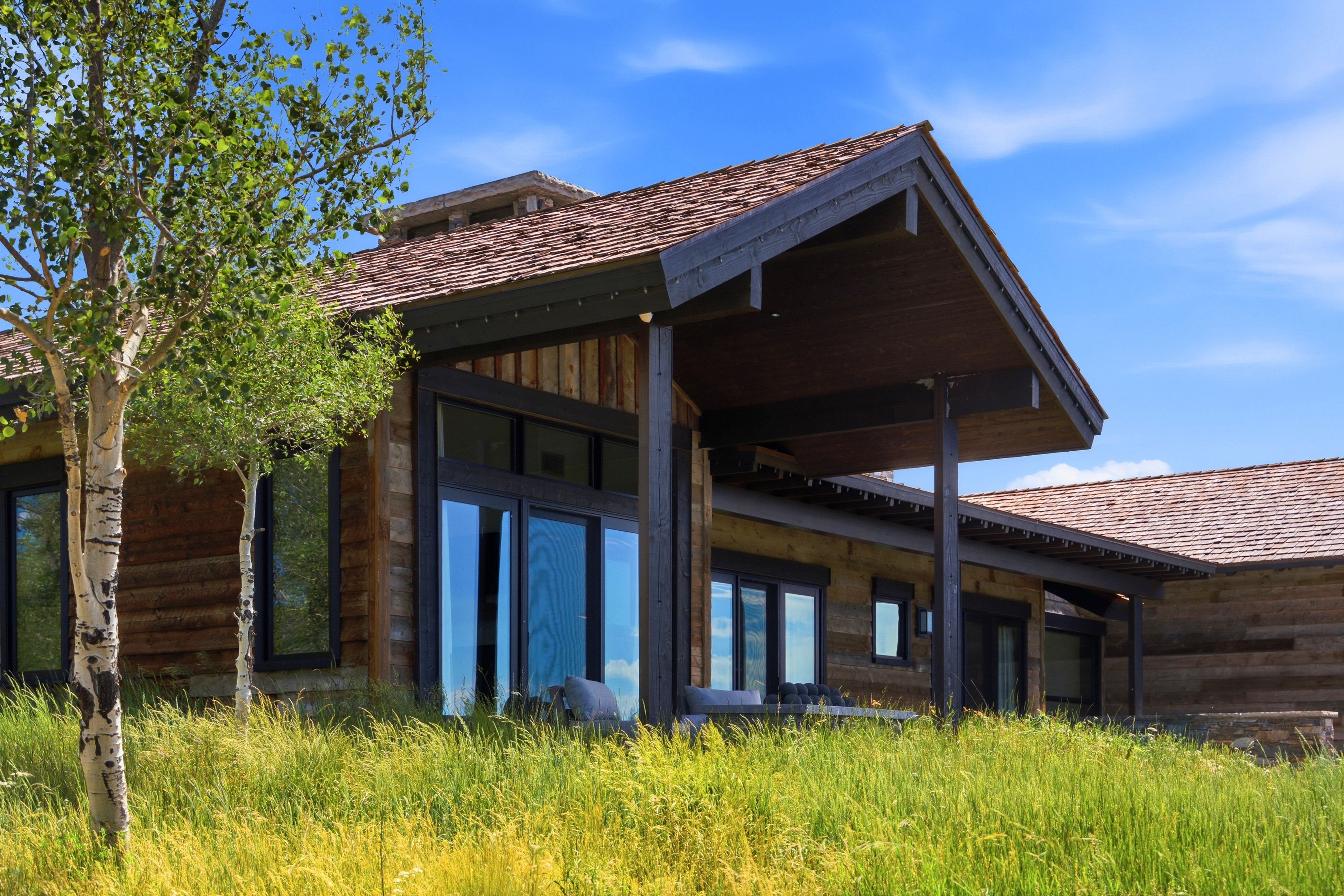 Rustic wood-sided exterior featuring extensive glazing, a covered patio, and a shingle roof
