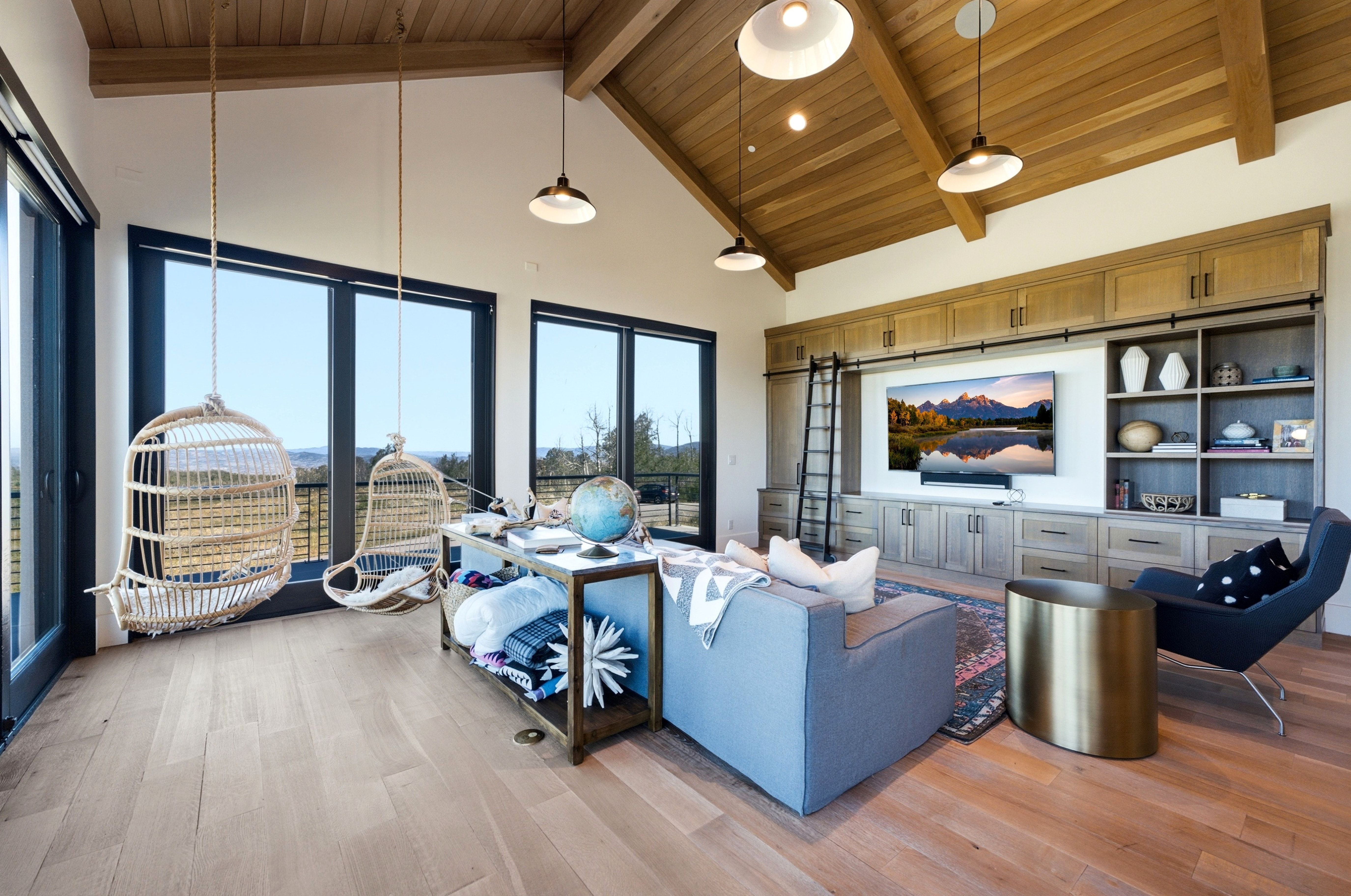Spacious room featuring light wood-finish flooring, a vaulted ceiling with exposed wood beams, and a built-in media center with shelving