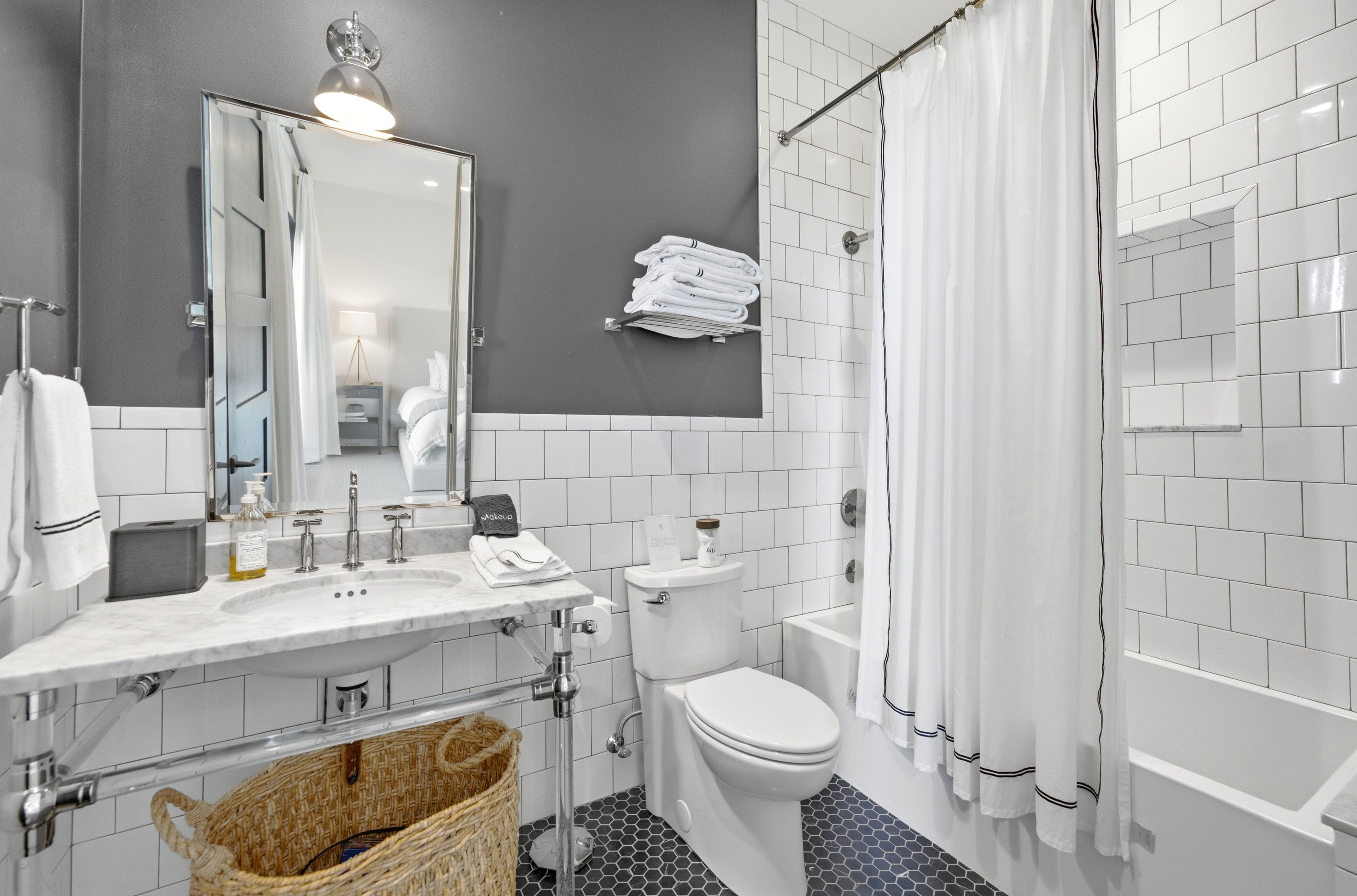 Bathroom featuring white subway tile, a chrome vanity with a marble-finish countertop, a single basin sink with chrome fixtures, a toilet, and a combination tub/shower with a built-in niche