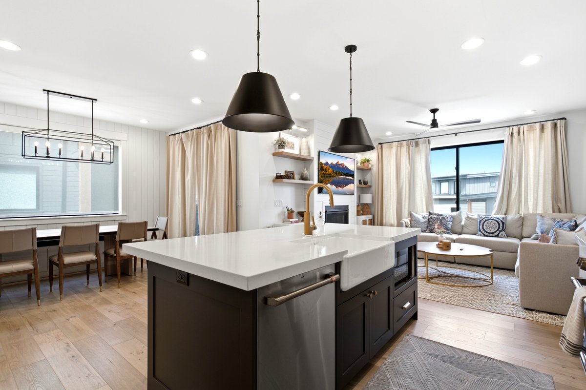 Open-concept living space featuring a central island with a white countertop and farmhouse sink, wood-finish flooring, recessed lighting, and a dining area with a linear chandelier
