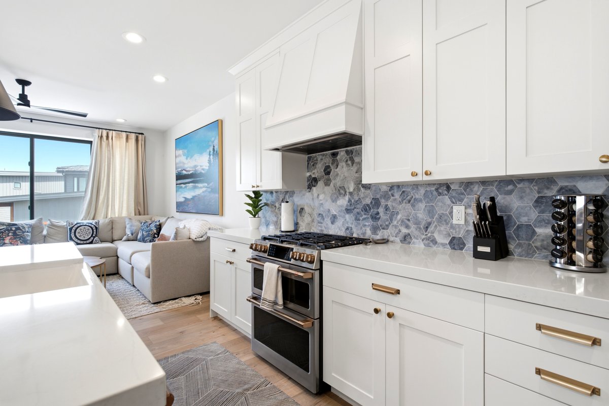 Contemporary kitchen featuring white cabinetry, light-toned countertops, and a hexagonal blue and gray tile backsplash