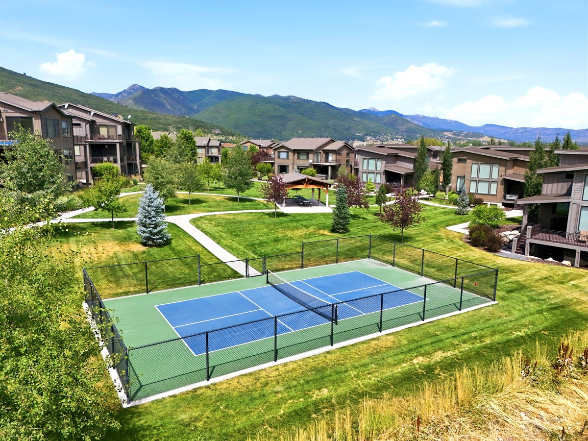 Fenced pickleball court with blue and green surfacing, surrounded by manicured lawns and mature trees