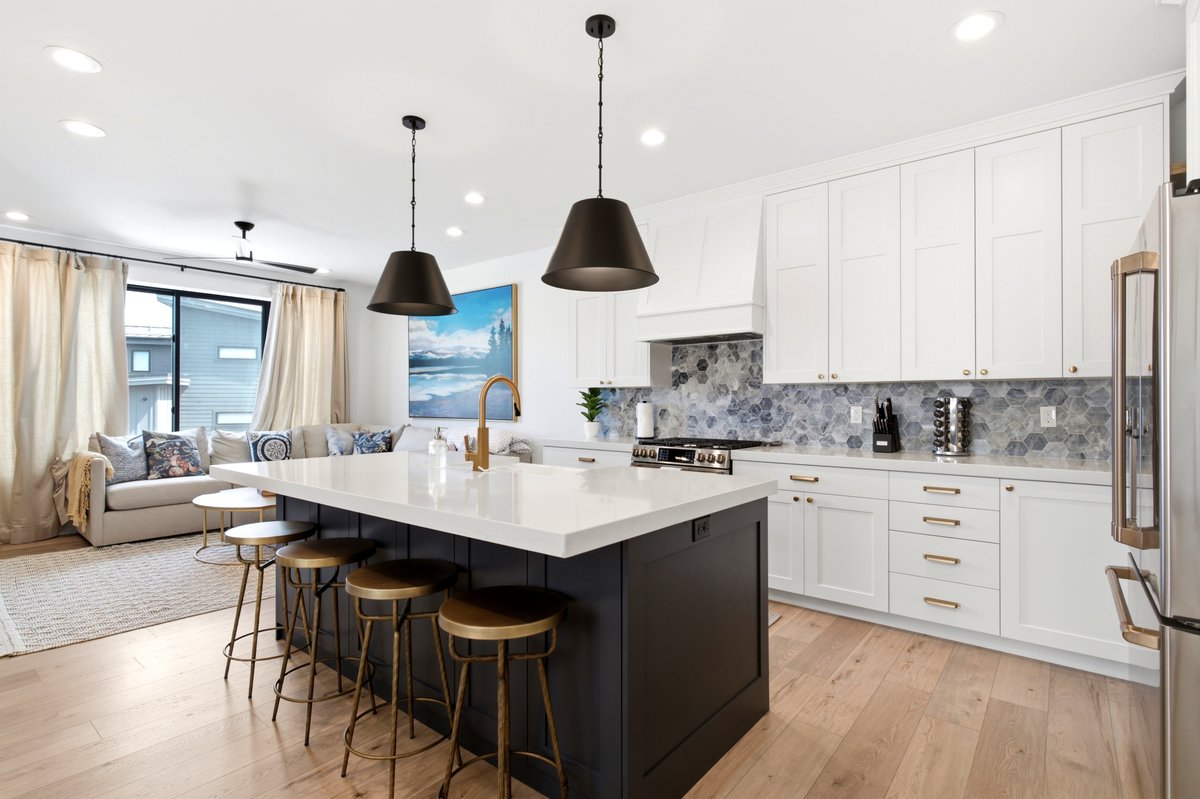 Kitchen featuring a large central island with seating, white shaker cabinetry, patterned tile backsplash, and light wood-finish flooring