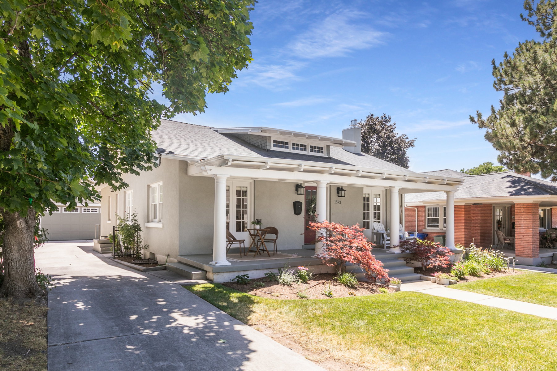 Inviting single-story residence featuring a covered front porch with white columns, a dormer with multiple windows, and a red front door