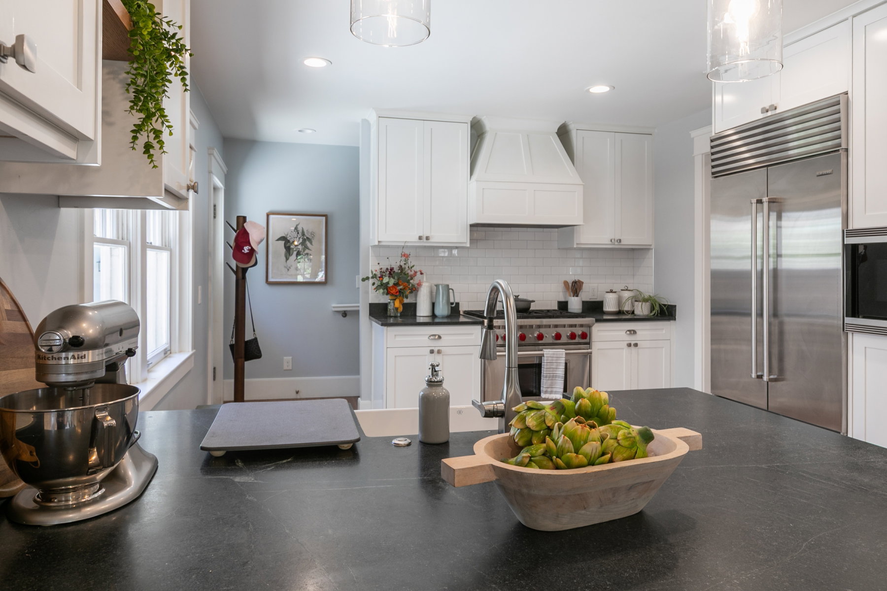 Kitchen featuring white shaker cabinetry, dark countertops, white subway tile backsplash, stainless steel appliances, and an island with an undermount sink