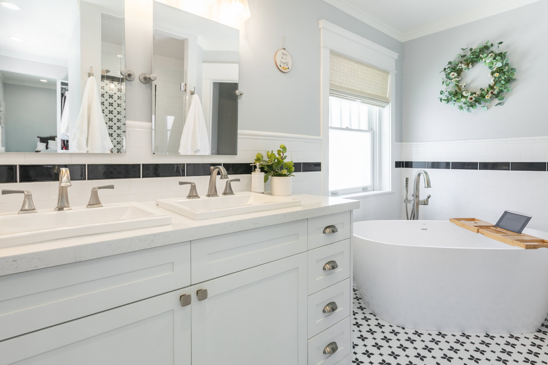 Bathroom featuring a freestanding soaking tub, dual vanity with undermount sinks, patterned floor tile, and a large window with privacy blind