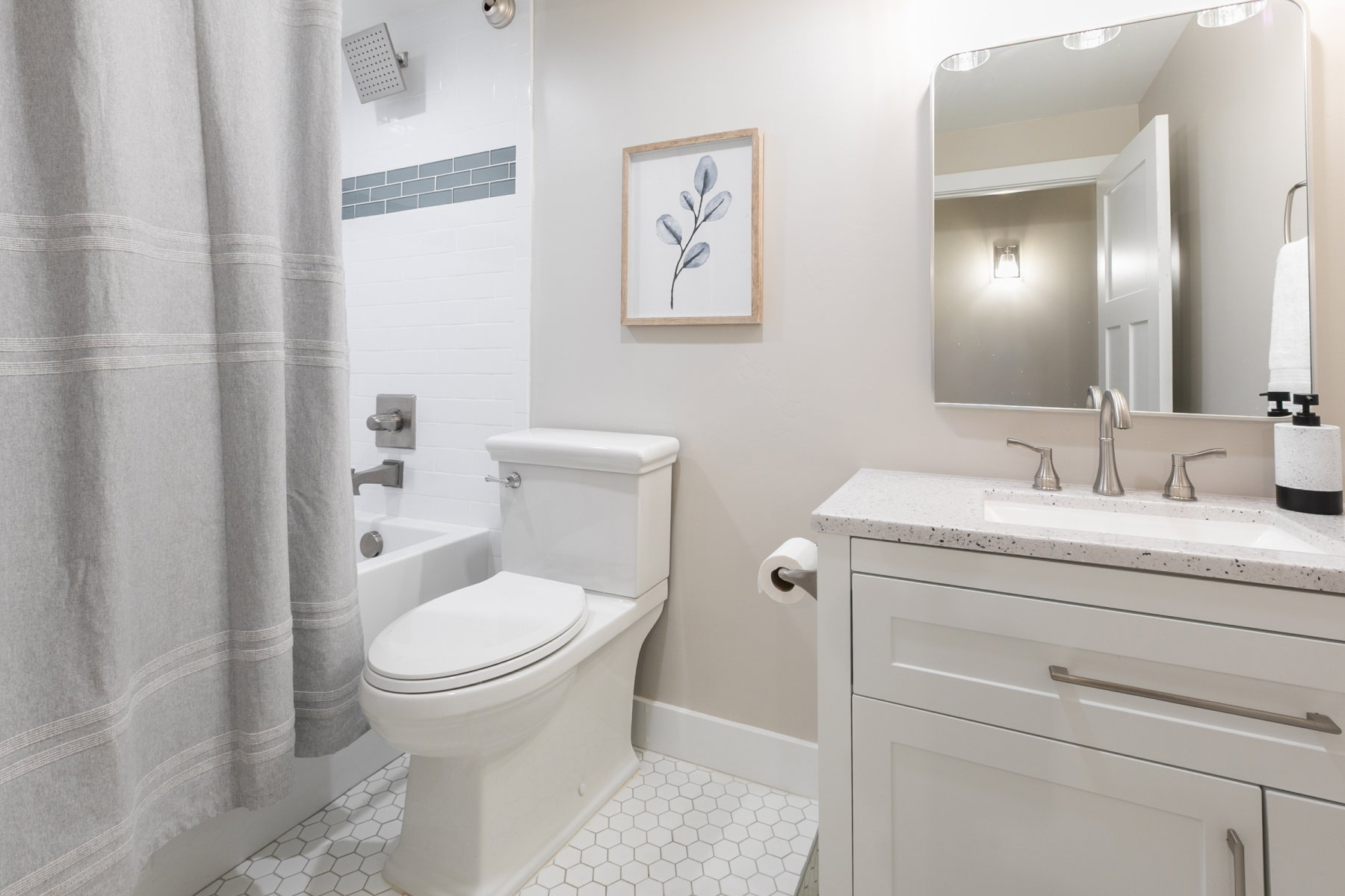 Bathroom featuring white hex tile flooring, a white vanity with a speckled countertop and undermount sink, a square-edged mirror with integrated lighting, and a bathtub with white subway tile surround and a gray accent tile band