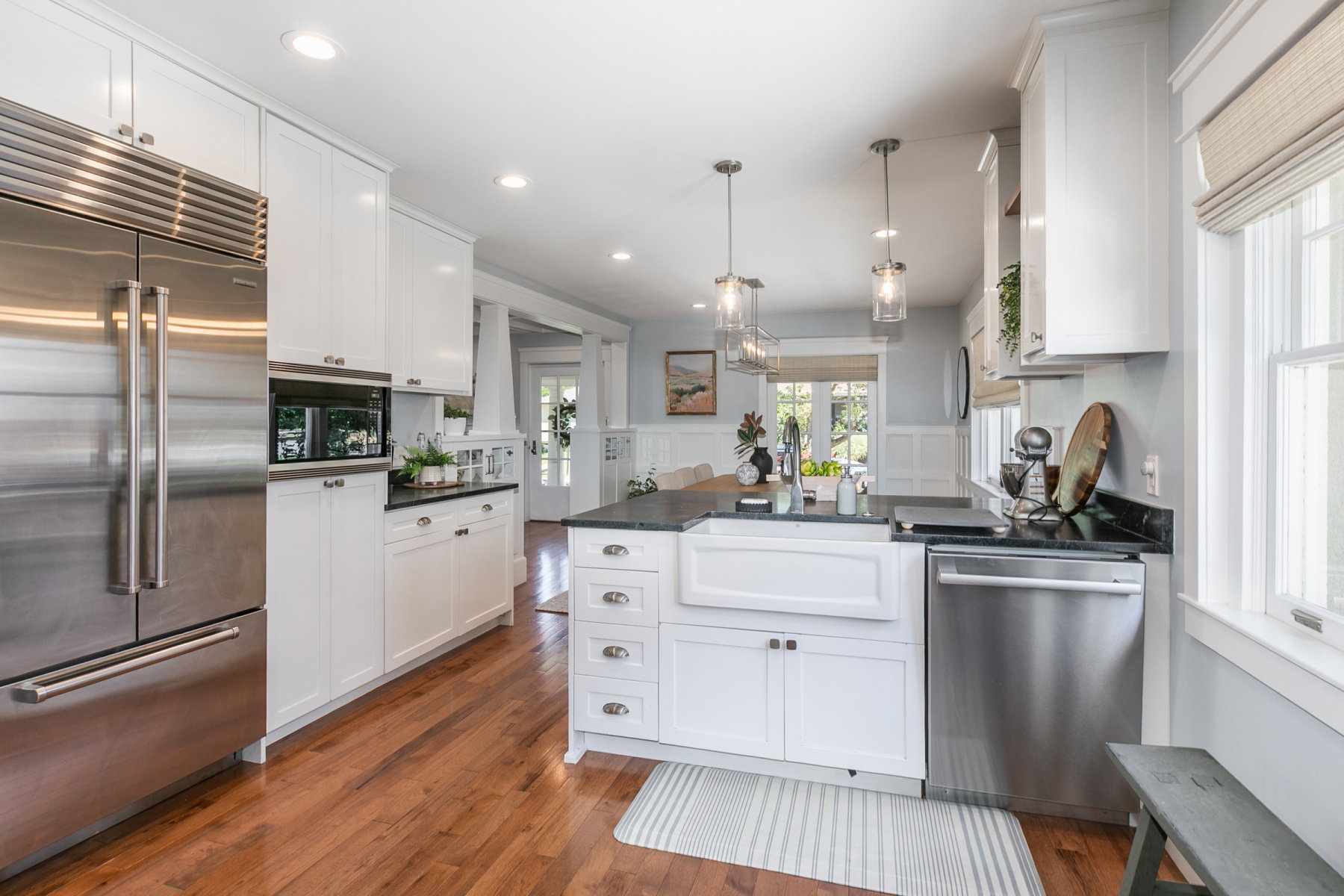 Kitchen featuring white cabinetry, dark countertops, a farmhouse sink, stainless steel appliances, and wood-finish flooring