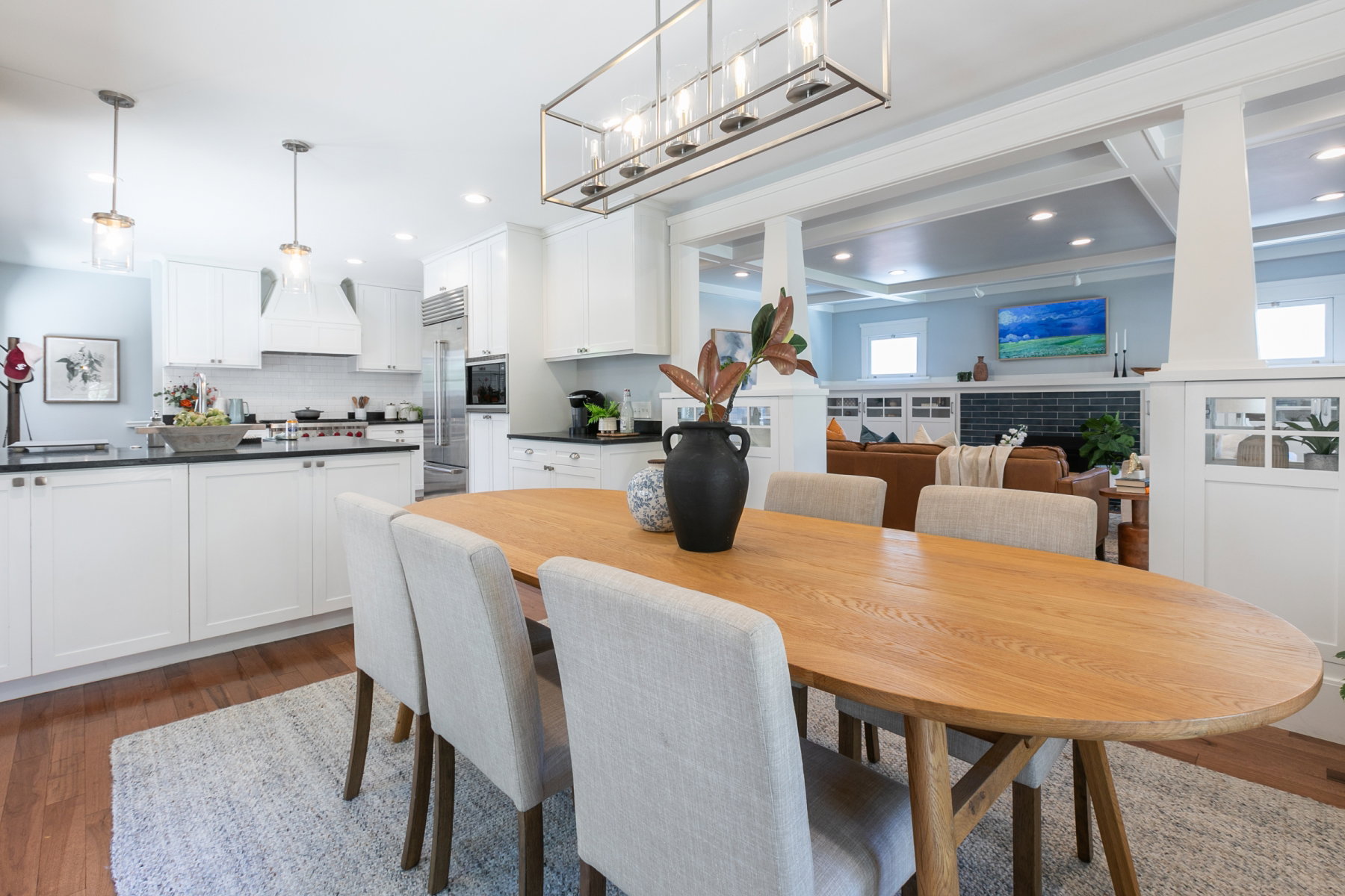 Open-concept dining area with wood-finish flooring, a contemporary linear chandelier, and decorative columns