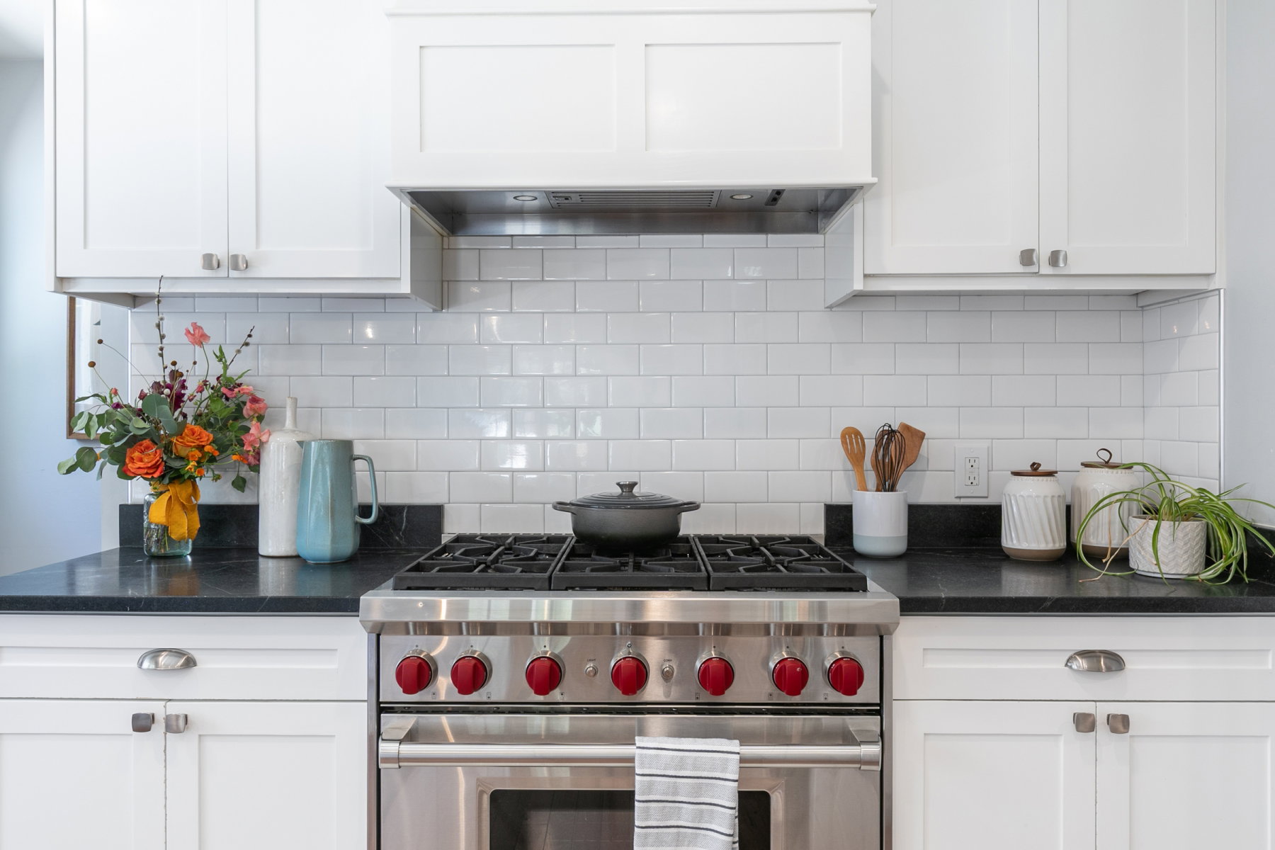 Contemporary kitchen featuring a stainless steel range with red accent knobs, white shaker cabinetry, and dark countertops