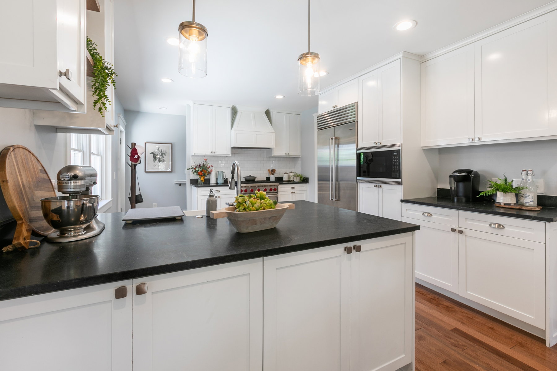 Contemporary kitchen featuring a substantial island with a dark countertop, white shaker-style cabinetry, stainless steel appliances, recessed lighting, and wood-finish flooring