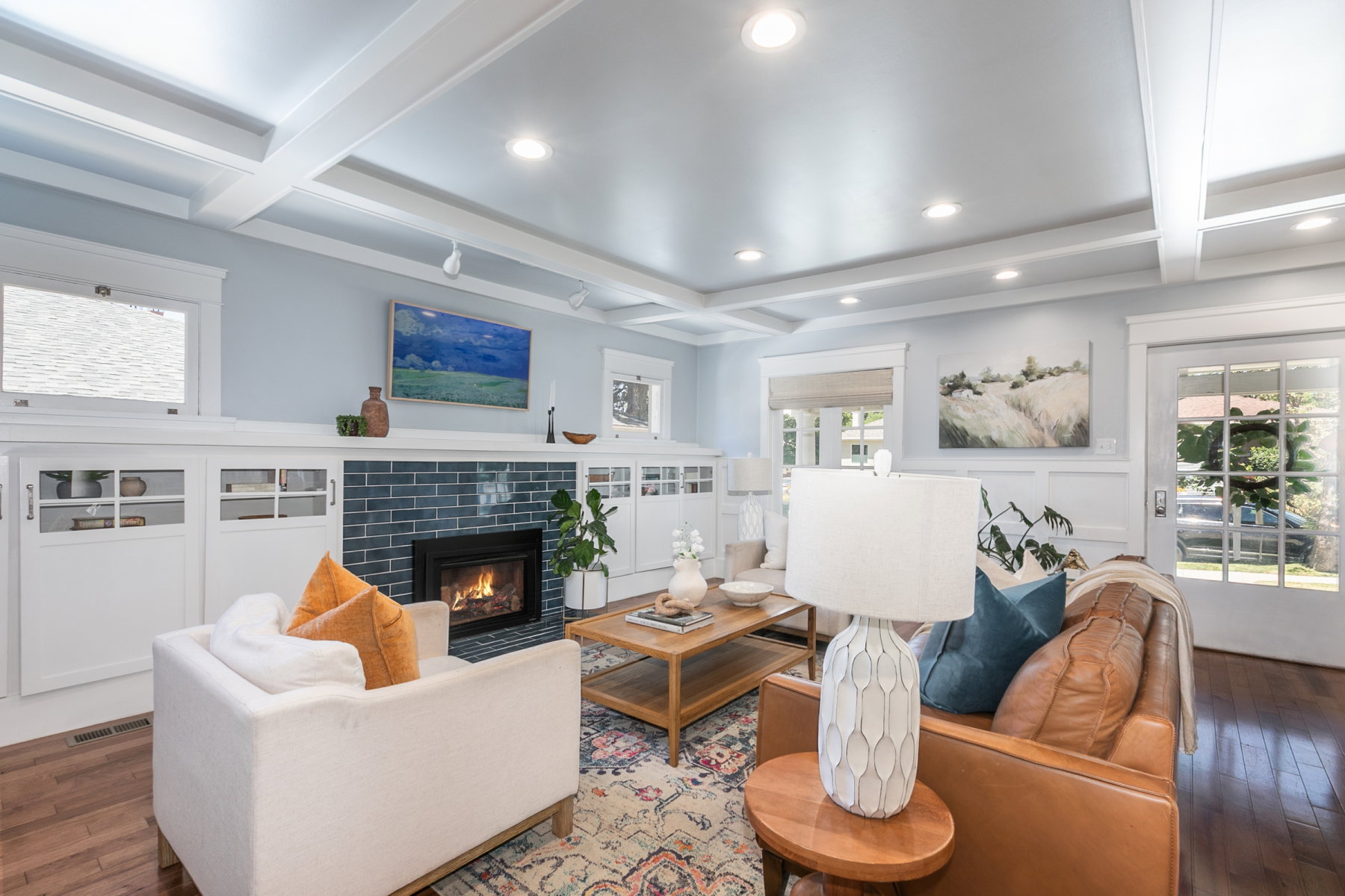 Living area featuring a fireplace with blue tile surround, wood-finish flooring, coffered ceiling, recessed lighting, and built-in cabinetry with glass-front doors