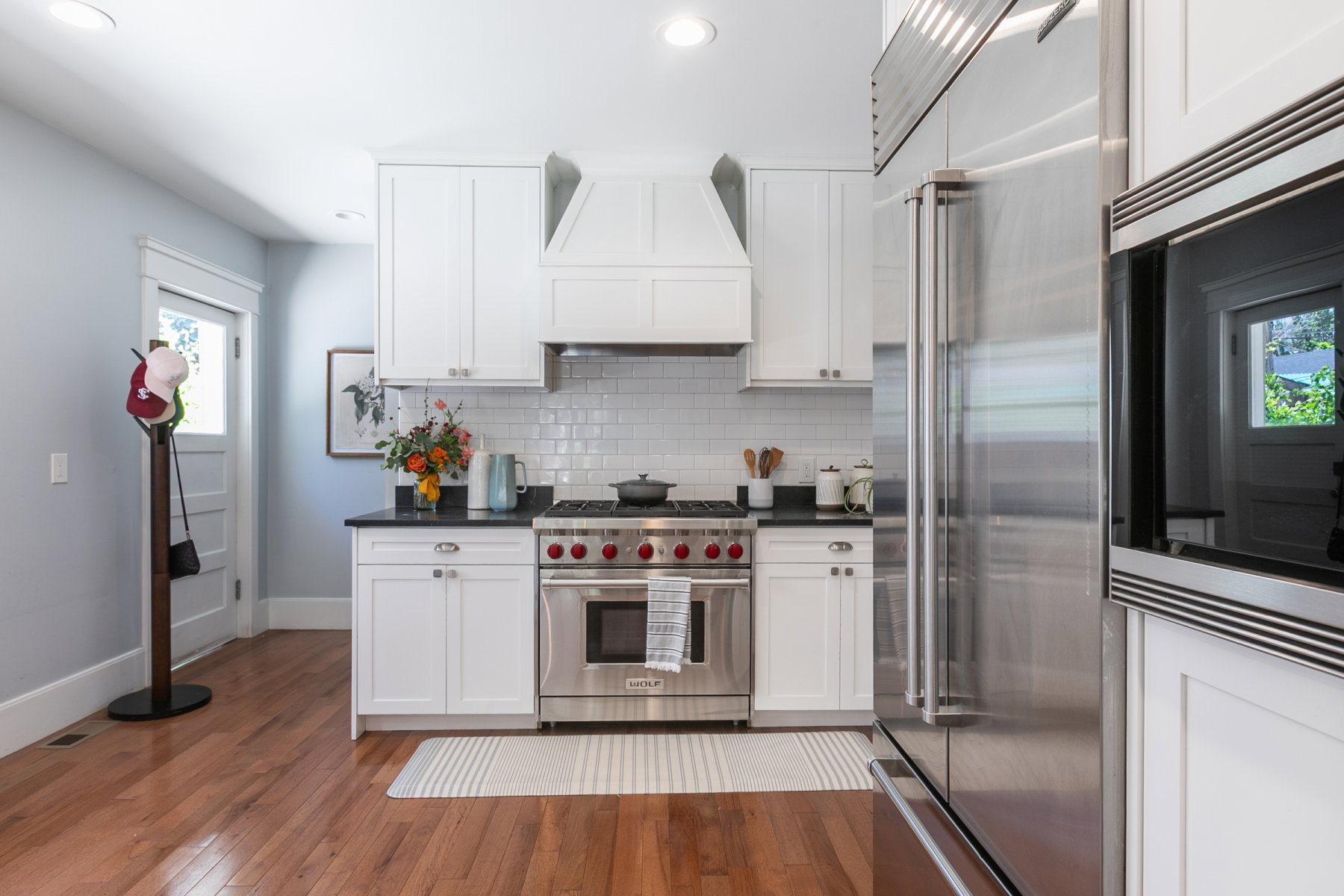 Modern kitchen featuring white shaker cabinetry, stainless steel appliances, black countertops, a subway tile backsplash, and wood-finish flooring