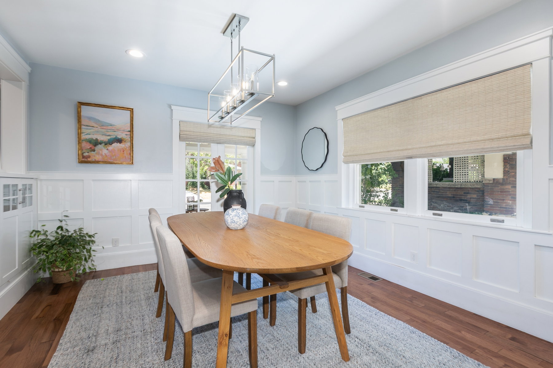 Dining area featuring hardwood flooring, extensive white wainscoting, and a linear pendant light fixture