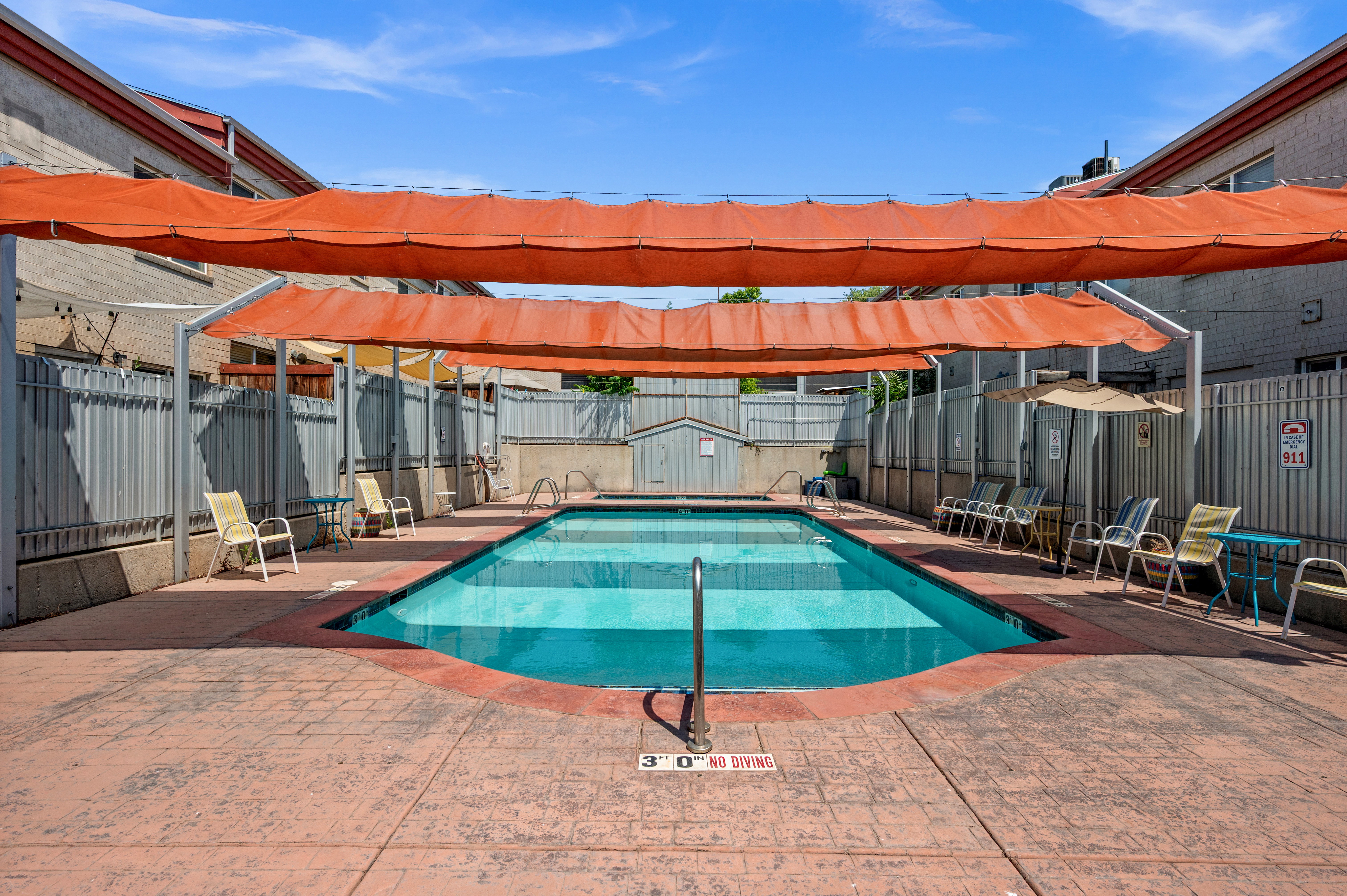 Outdoor swimming pool featuring a patterned concrete deck and overhead sun shades
