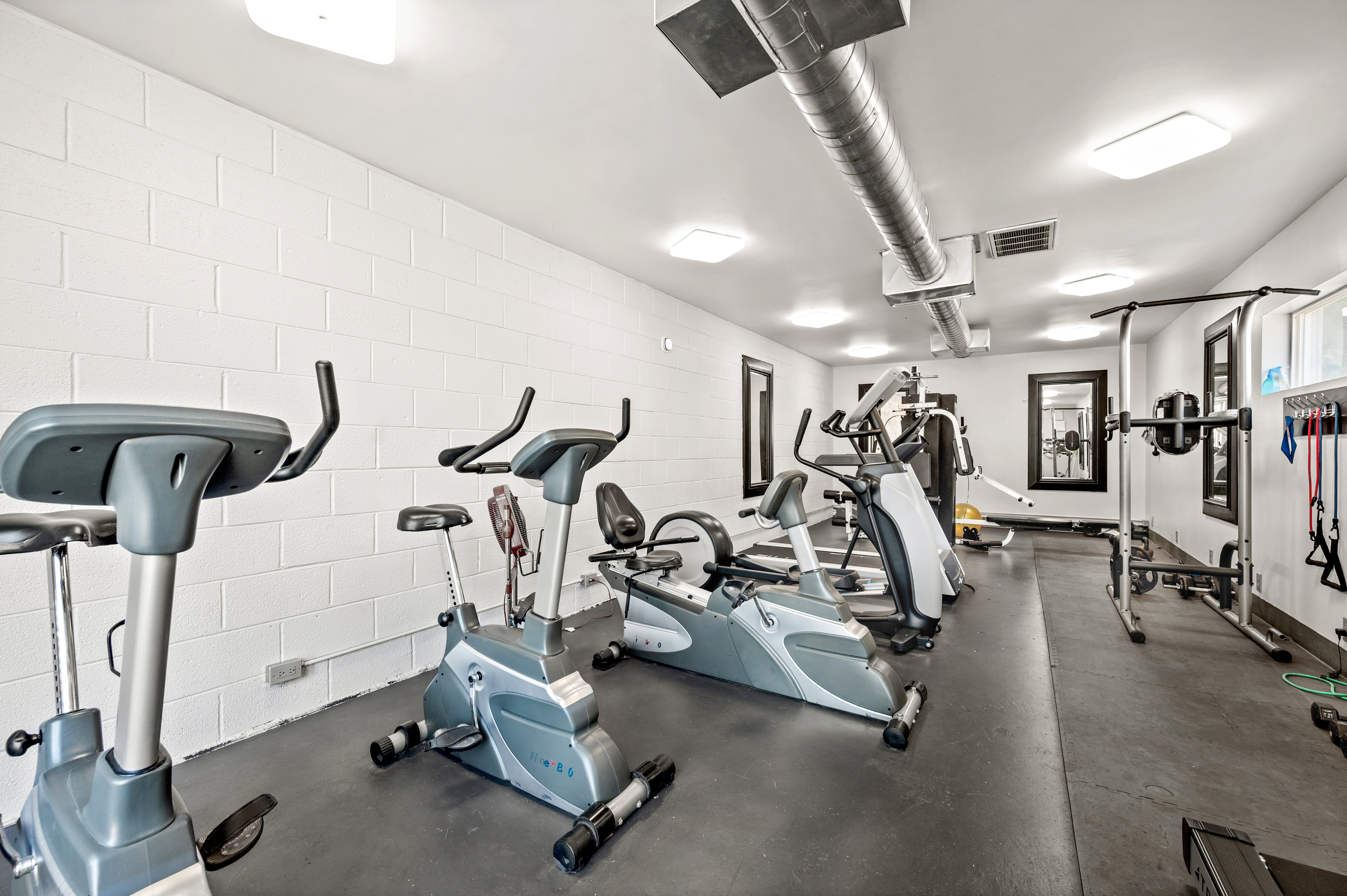 Fitness room featuring white block walls, dark flooring, exposed ductwork, and recessed lighting