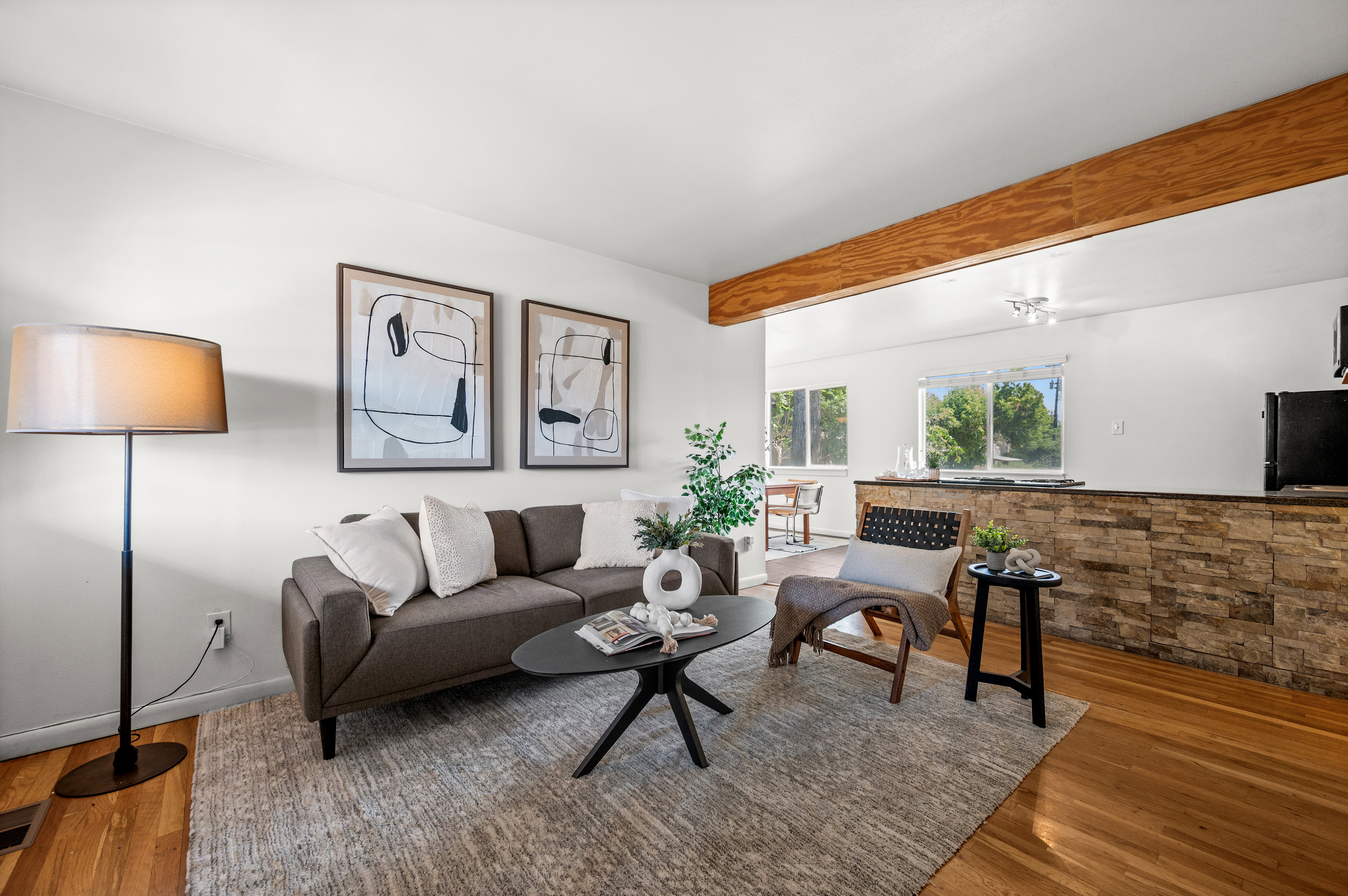 Living area with hardwood flooring, a stone-finish half-wall, and an exposed wood beam