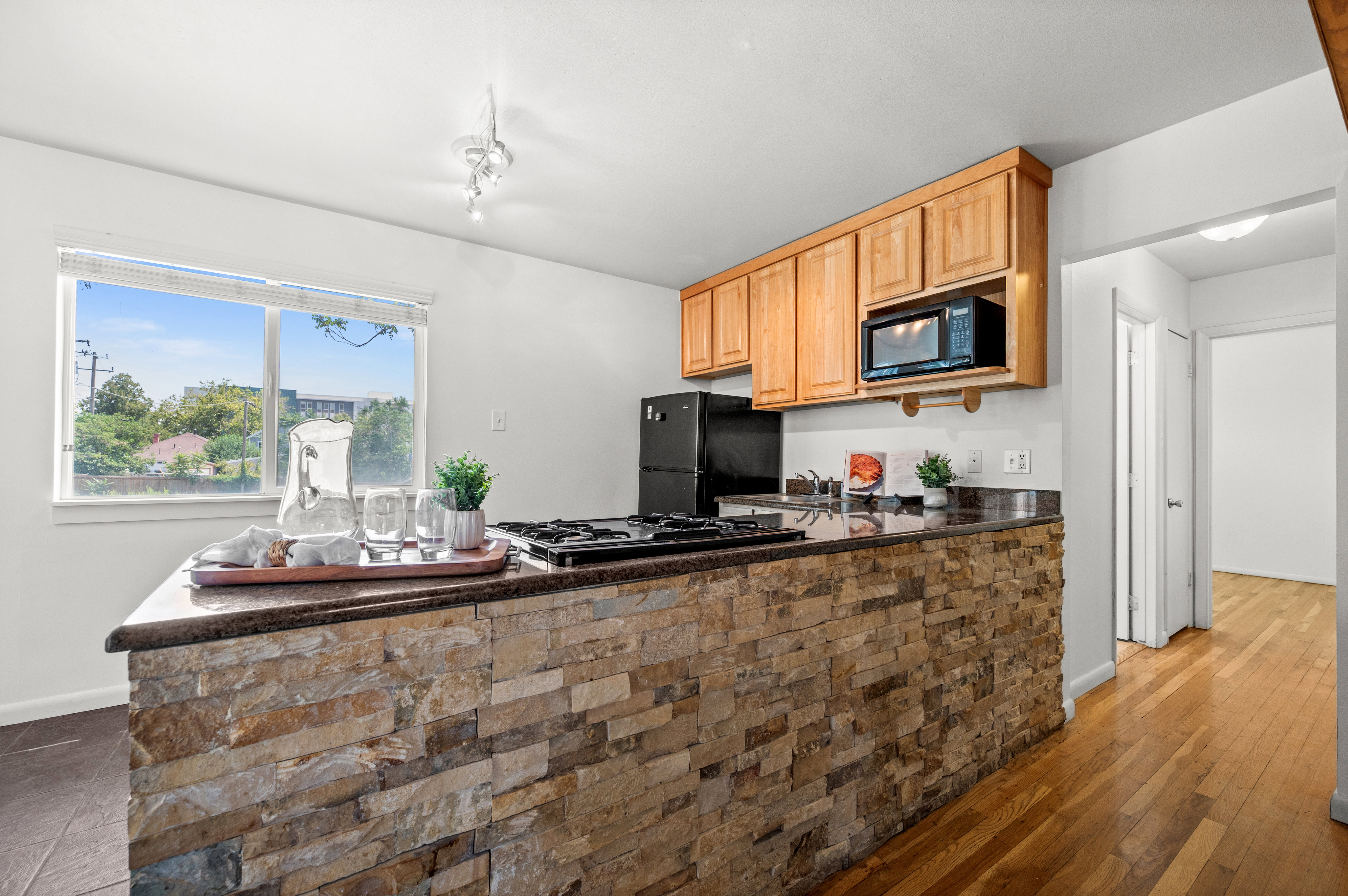 Kitchen featuring a stone-faced island with integrated cooktop, a dark countertop, and light wood cabinetry