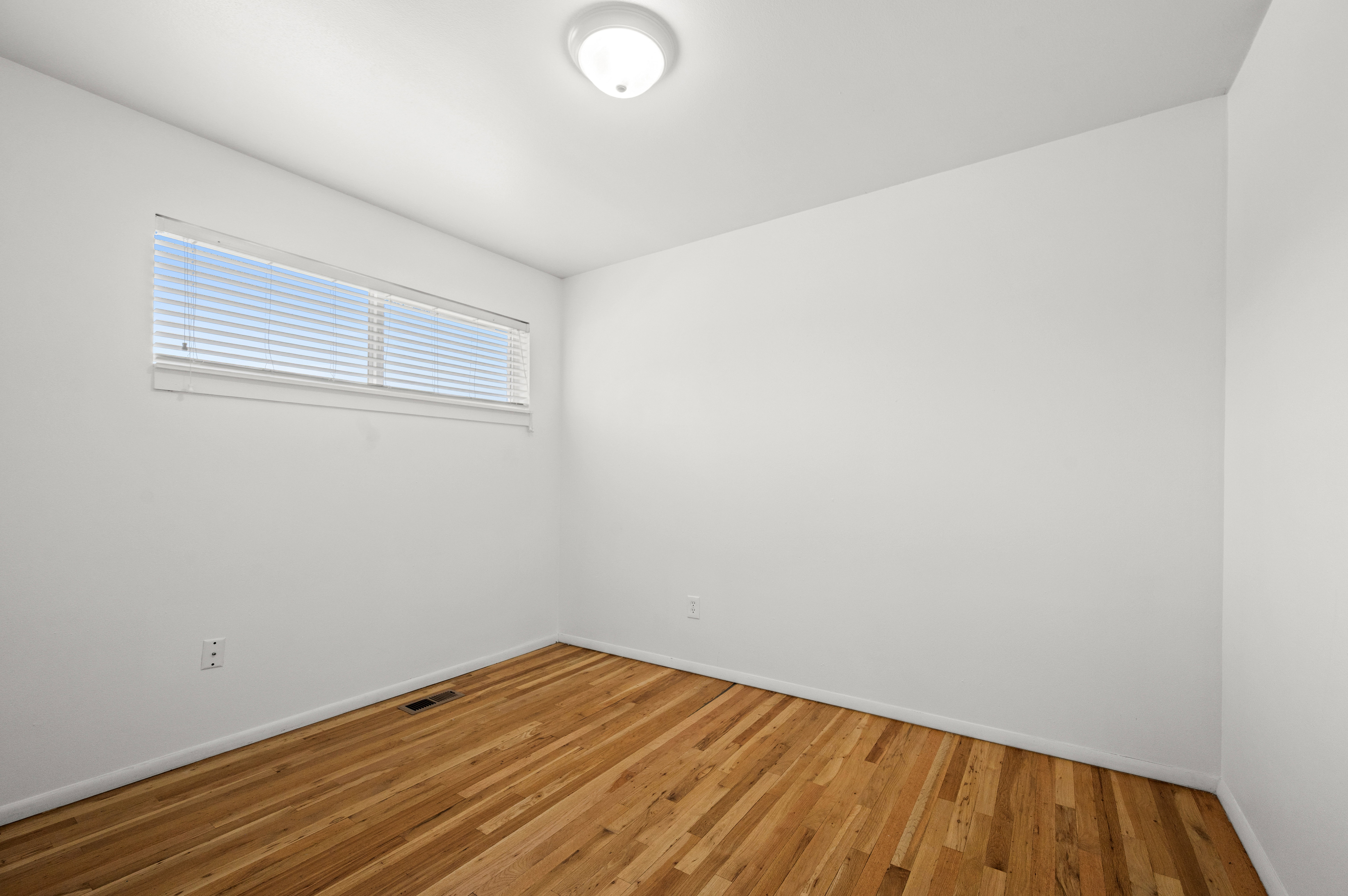 Room featuring wood-finish flooring, white walls, and a horizontal window with blinds