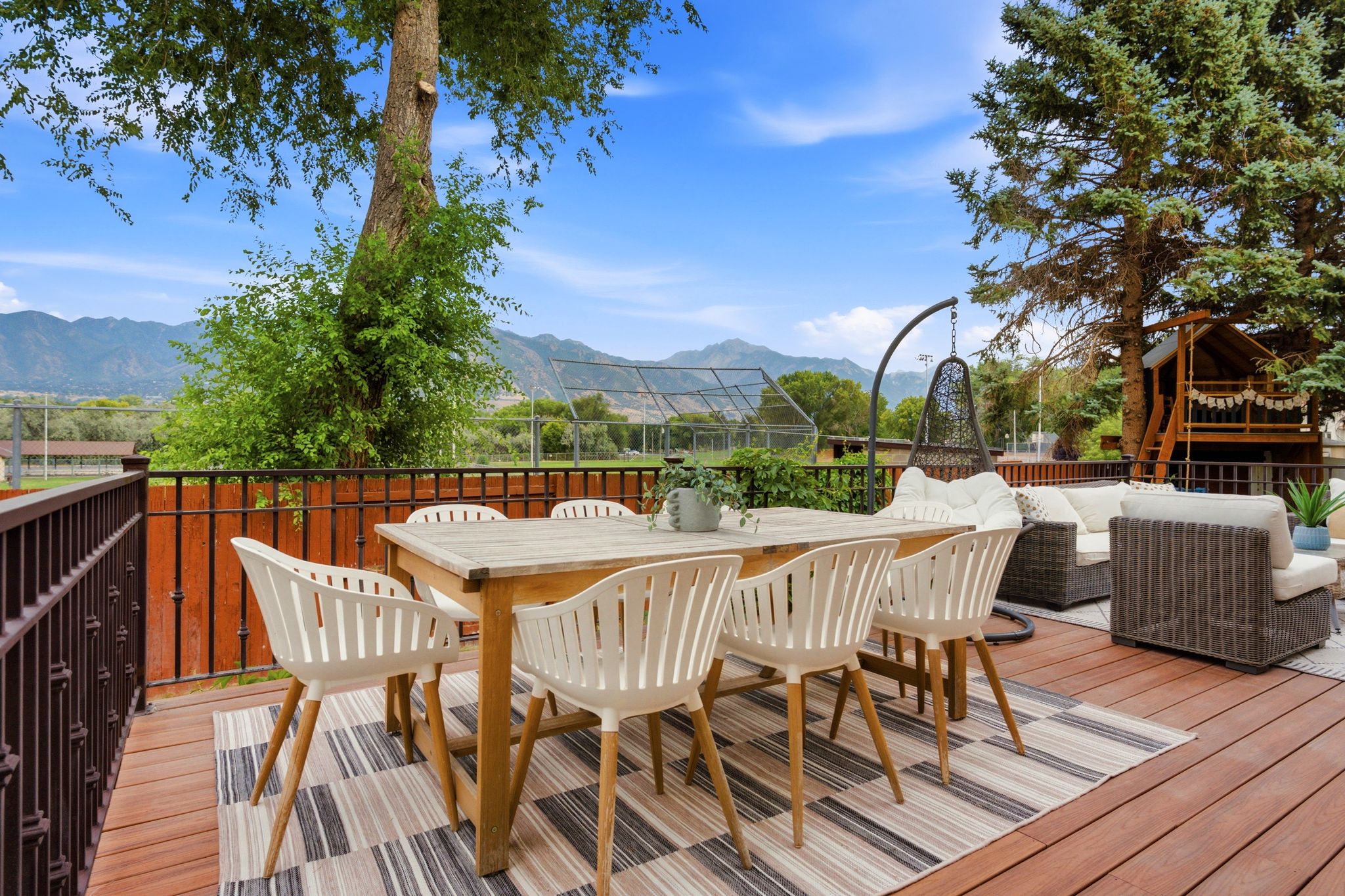 Expansive outdoor deck featuring wood-finish flooring, a metal railing, and mature trees providing natural shade