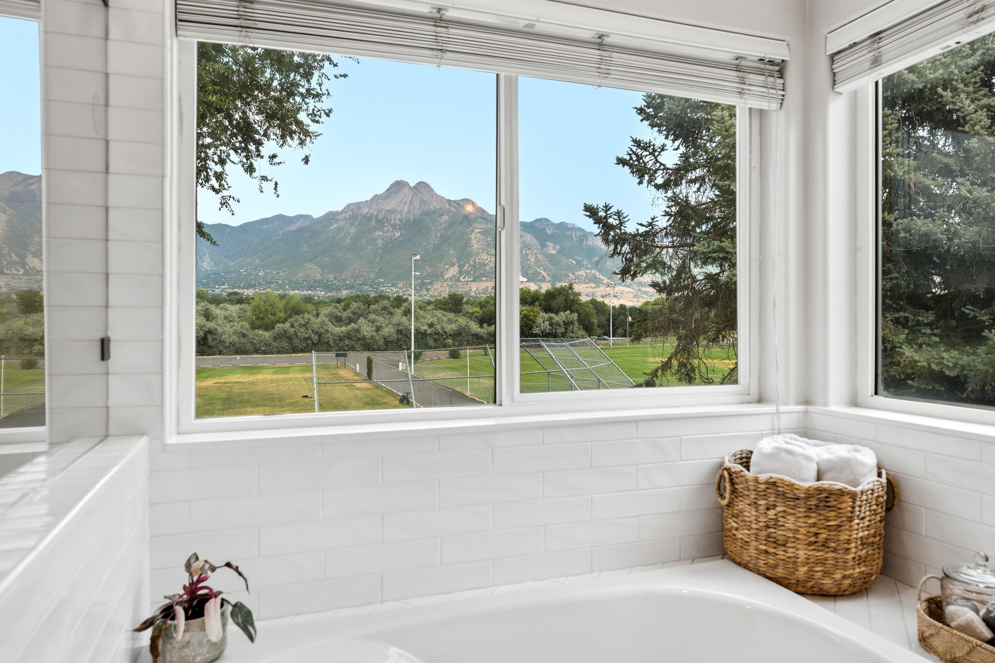 Built-in soaking tub featuring white subway tile surround, multiple windows, and mountain scenery