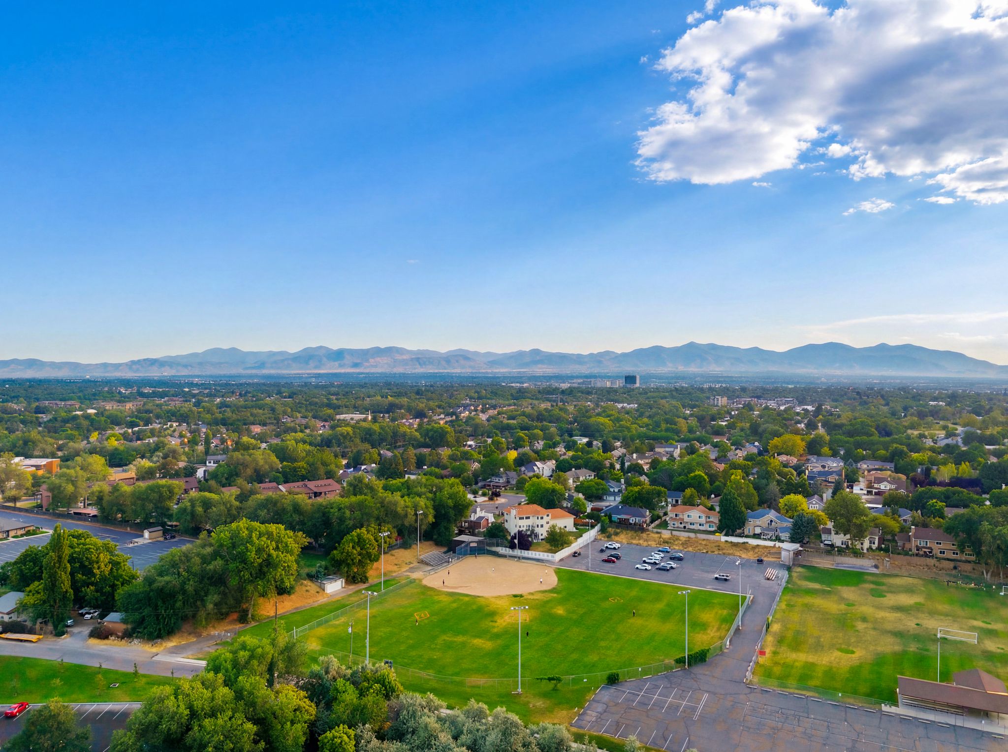 Aerial perspective showcasing a residential area with extensive tree canopy, a baseball field, and surrounding parking facilities