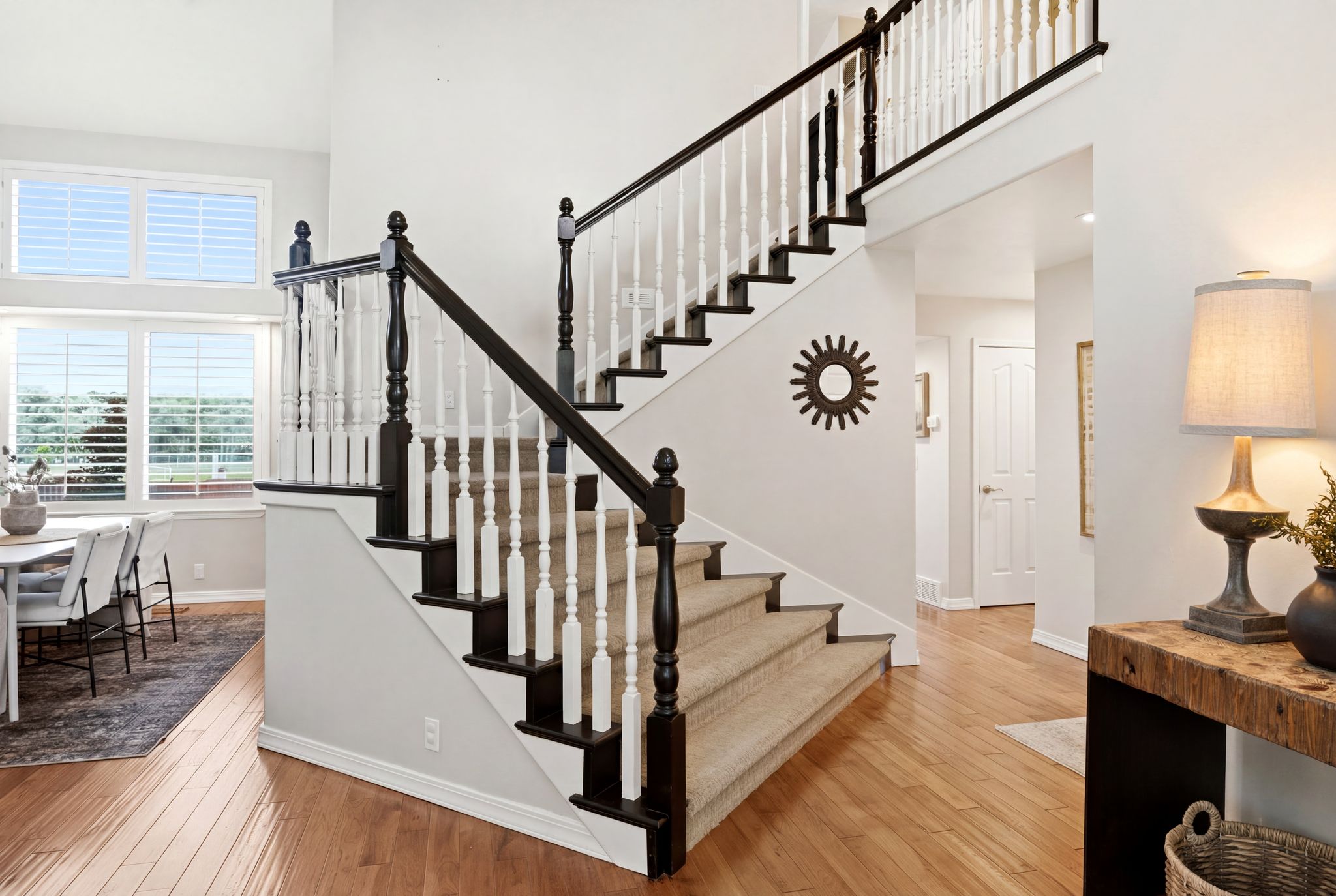 Two-story entryway with hardwood flooring and a carpeted staircase featuring dark wood newel posts and handrails contrasting with white balusters