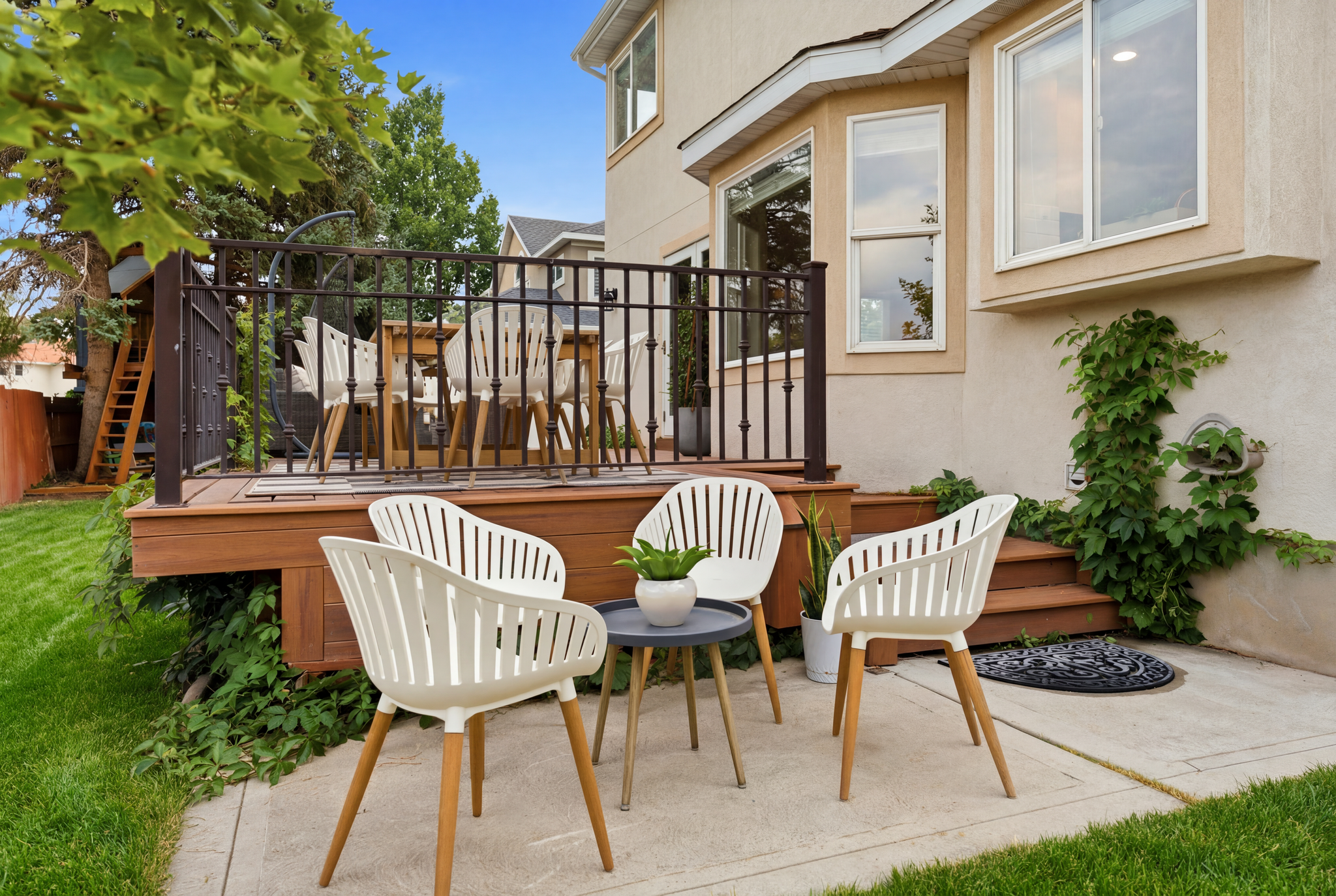 Expansive backyard featuring a manicured lawn, a multi-level wood-finish deck with black metal railings, and a concrete patio area