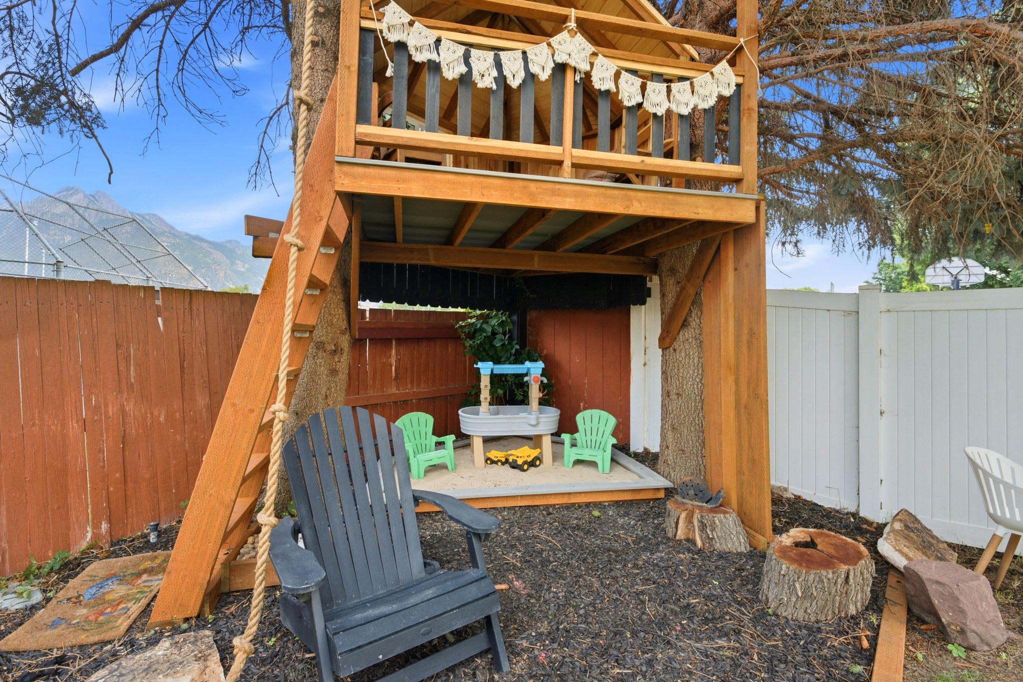 Custom-built multi-level treehouse featuring a rope ladder, wood staircase, and an enclosed lower-level sandbox