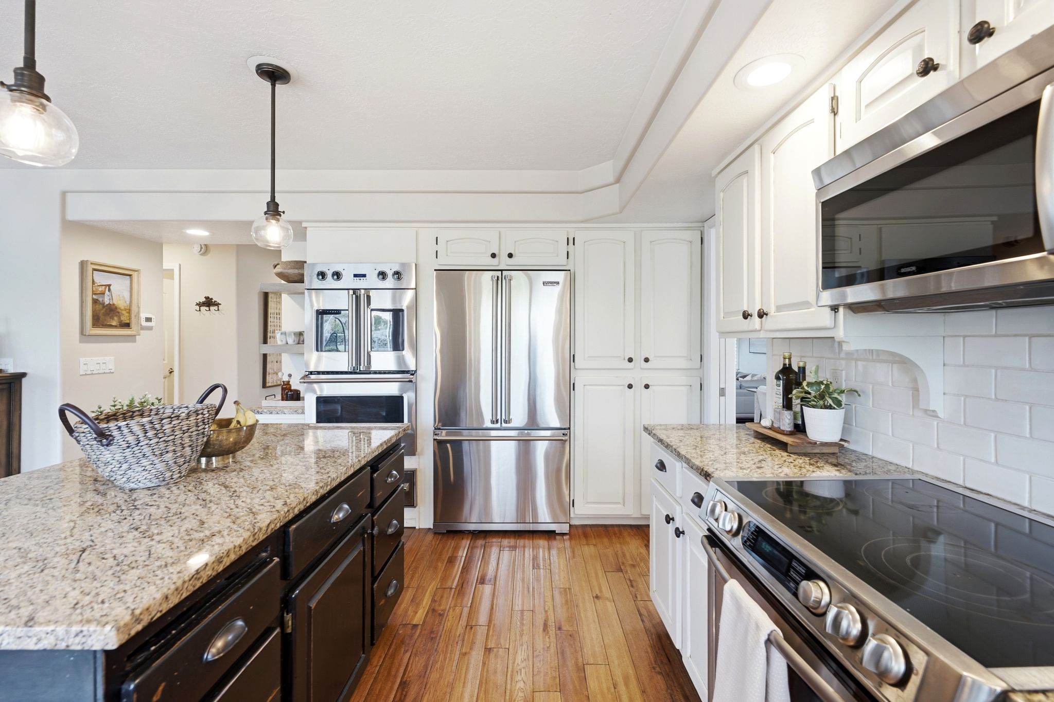 Gourmet kitchen featuring granite countertops, stainless steel appliances, white cabinetry, a subway tile backsplash, and wood-finish flooring