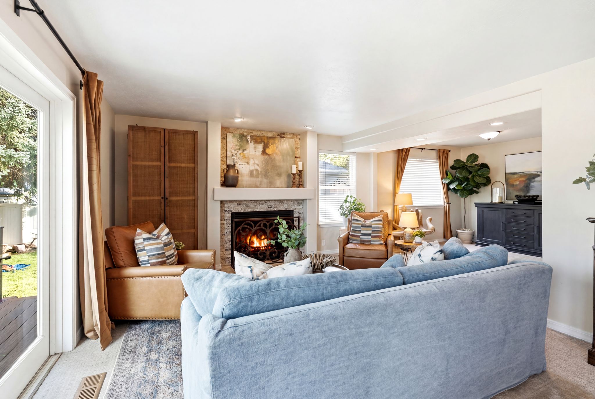 Spacious living area featuring a stone-faced fireplace with an ornate iron grate, built-in shelving, wood-finish flooring, and a glass-paneled exterior door opening to an outdoor deck