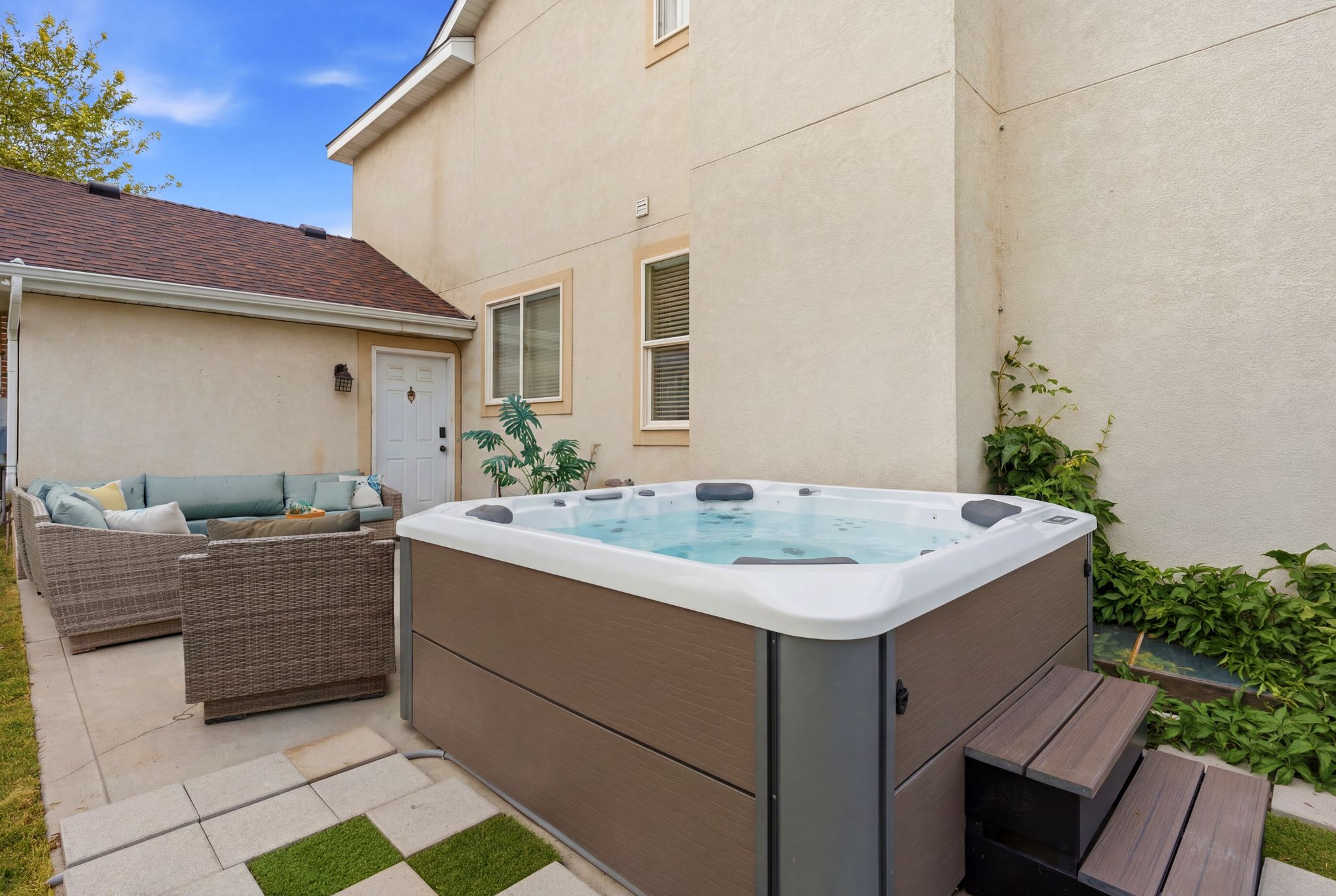 Private outdoor patio featuring a built-in hot tub with composite steps, an expansive concrete pad, and a checkerboard paver accent