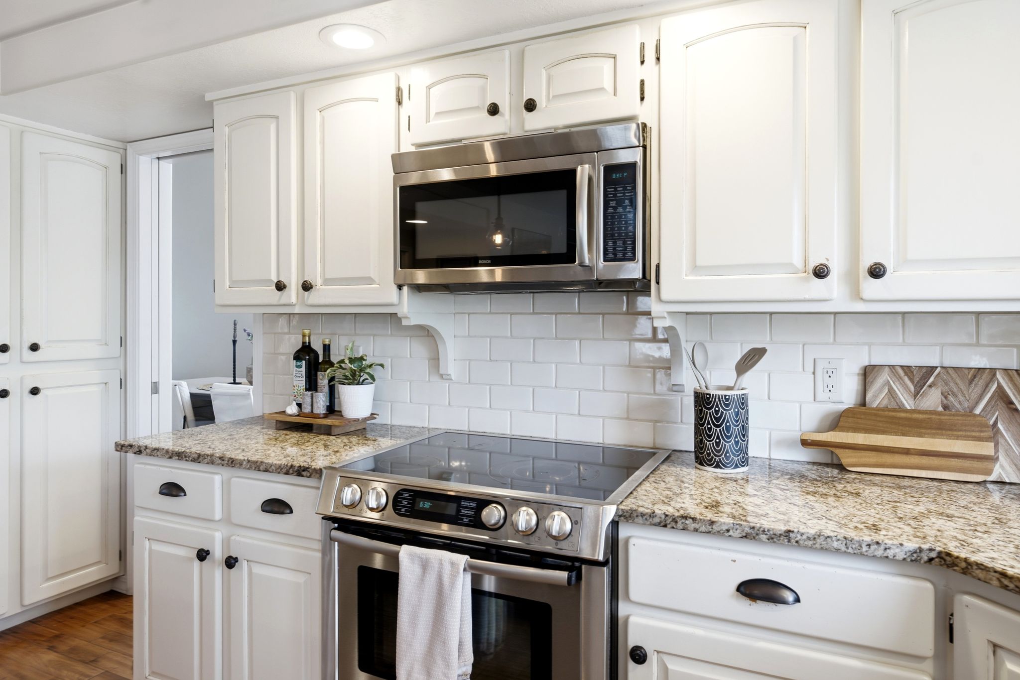 Modern kitchen featuring white cabinetry, granite countertops, a built-in stainless steel microwave, a stainless steel range, and a white subway tile backsplash