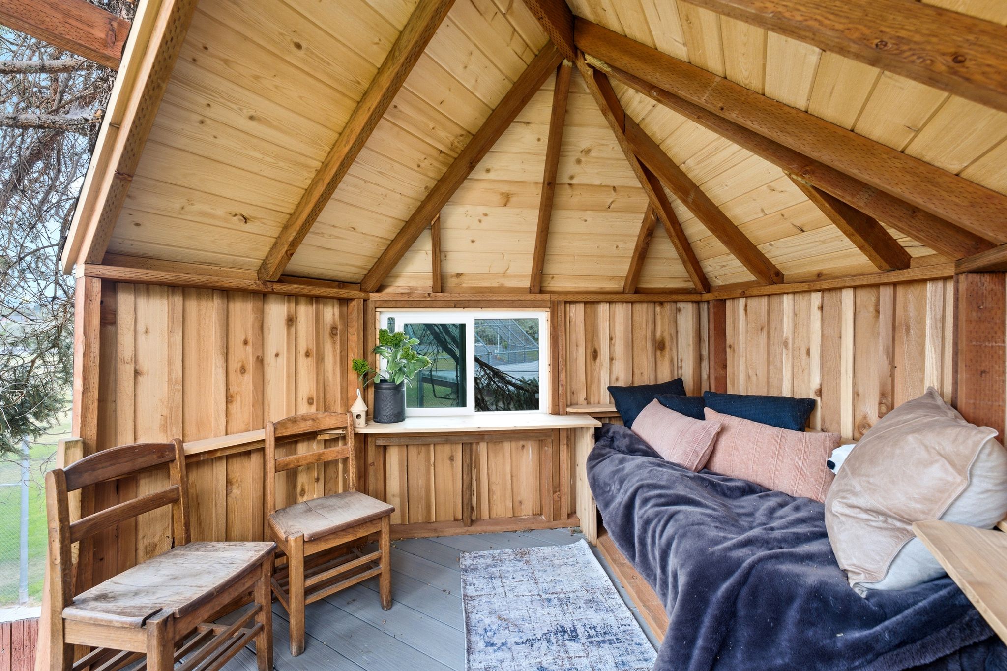 Wood-paneled interior space featuring a vaulted ceiling with exposed beams, a built-in daybed, and a fixed window