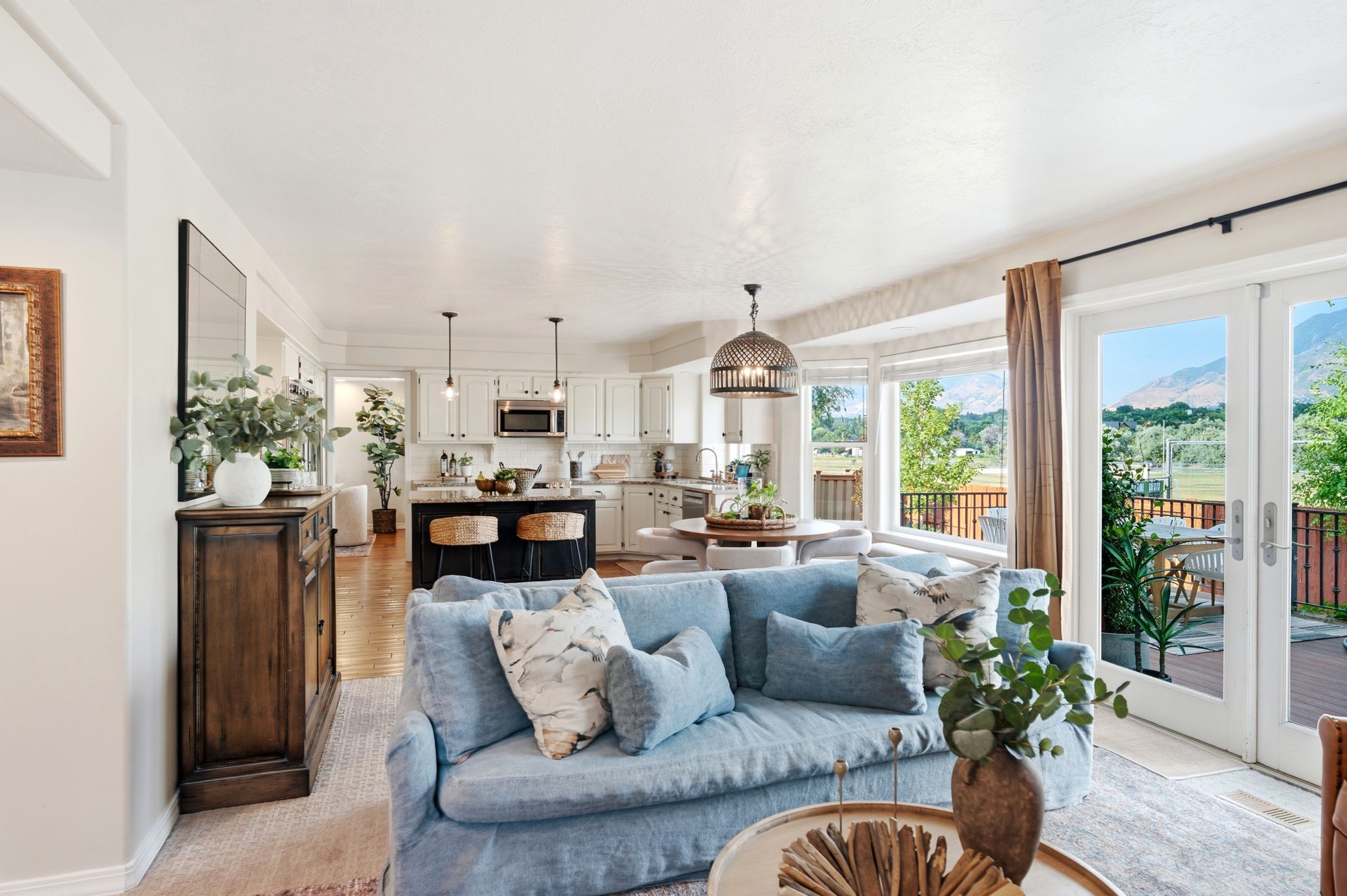 Open-concept living area featuring wood-finish flooring, a kitchen with white cabinetry and a dark island, and a dining area with a contemporary chandelier