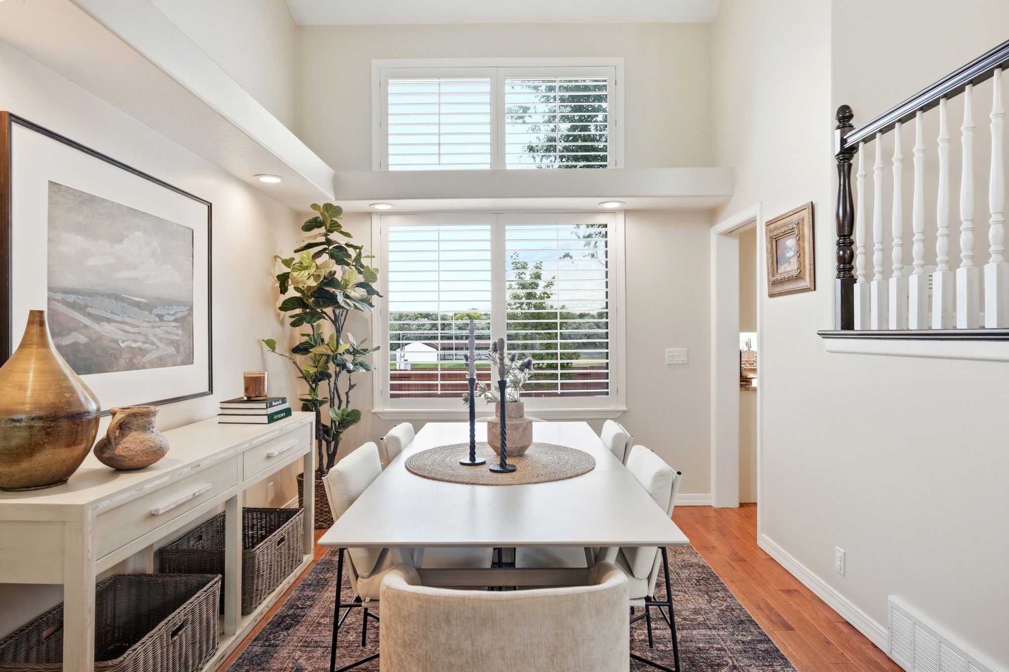 Dining area featuring a high ceiling, wood-finish flooring, two large windows with plantation shutters, recessed lighting, and a white console table with storage baskets