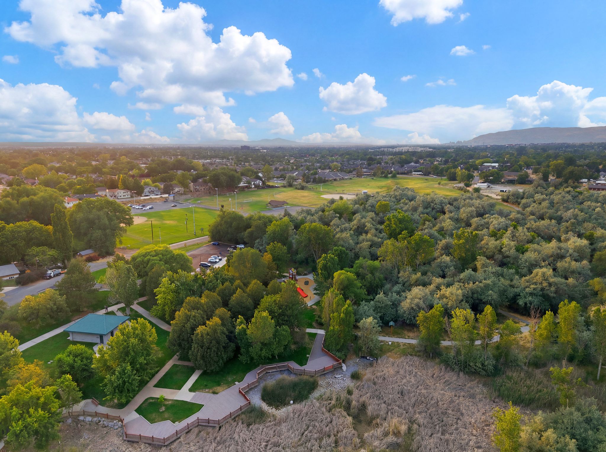 Expansive natural surroundings featuring abundant trees, a large grassy field, and a network of paved paths and wooden boardwalks