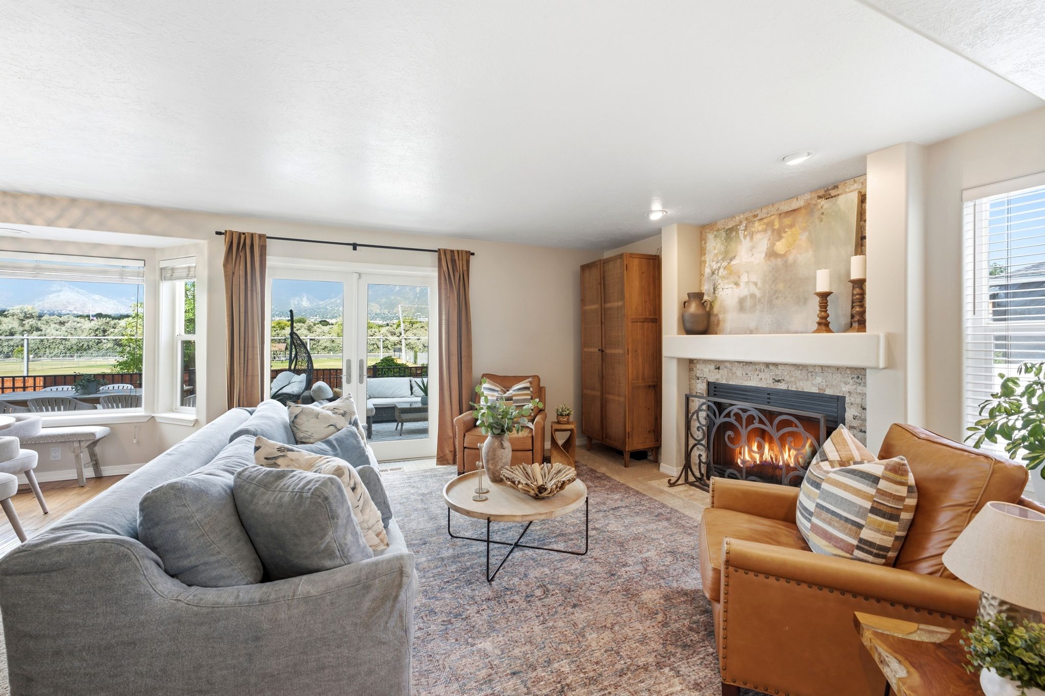 Living room featuring a built-in fireplace with a decorative screen and stone surround, large bay window, and glass sliding doors opening to an exterior deck