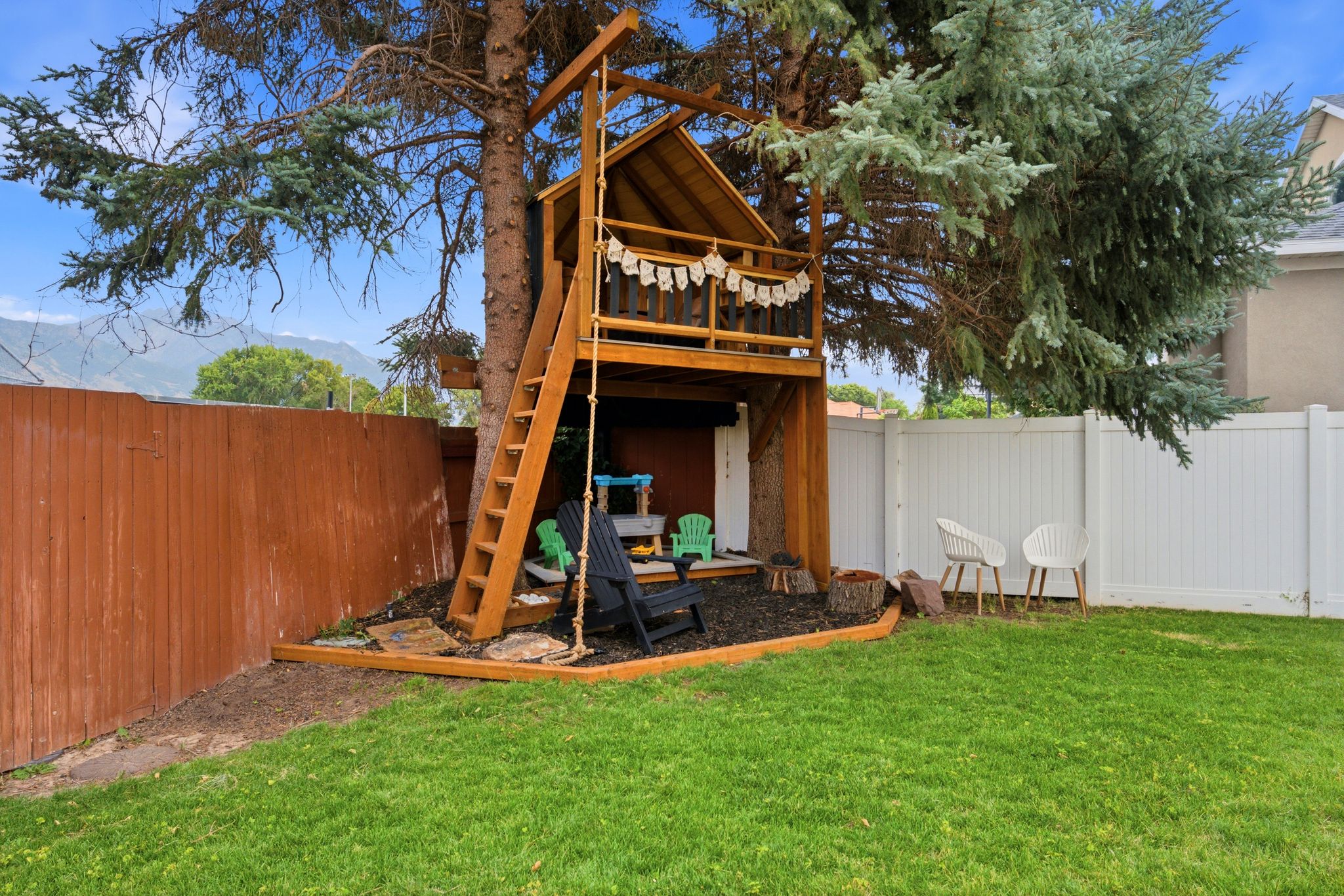 Expansive backyard featuring a manicured lawn, a built-in multi-level treehouse with a ladder, wood fencing, white vinyl fencing, and mature trees