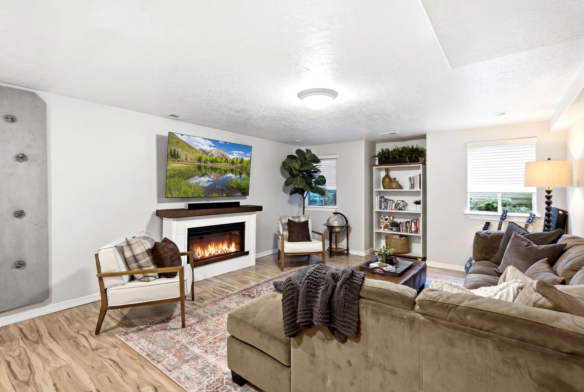 Living area featuring a wall-mounted television above an electric fireplace with a wood mantle, wood-finish flooring, a built-in shelving unit, and two windows with blinds