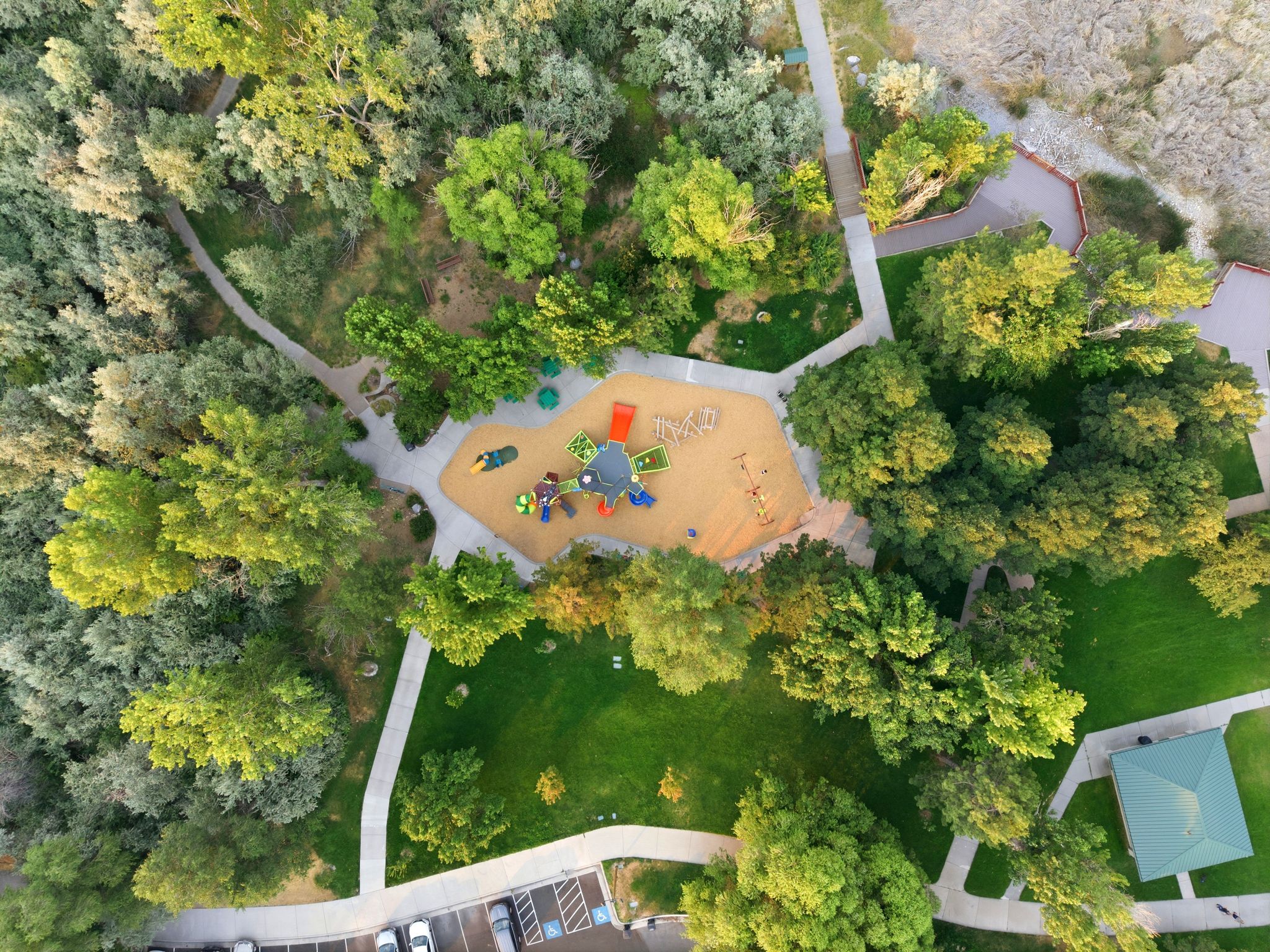 Expansive park area featuring a central playground with multiple structures, surrounded by mature trees and manicured green spaces