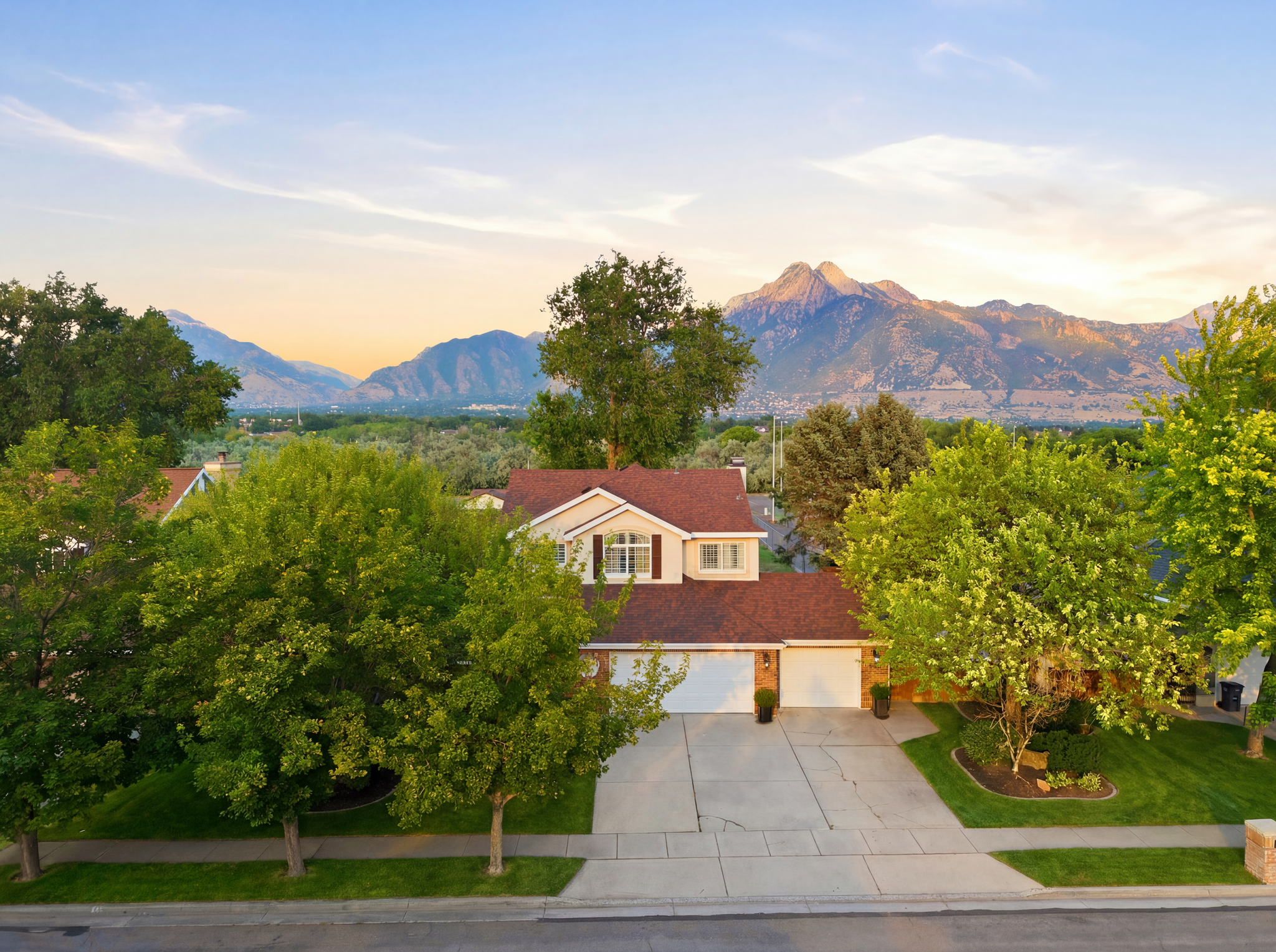 Two-story home with a brown shingle roof and beige siding, set against a backdrop of distant mountains