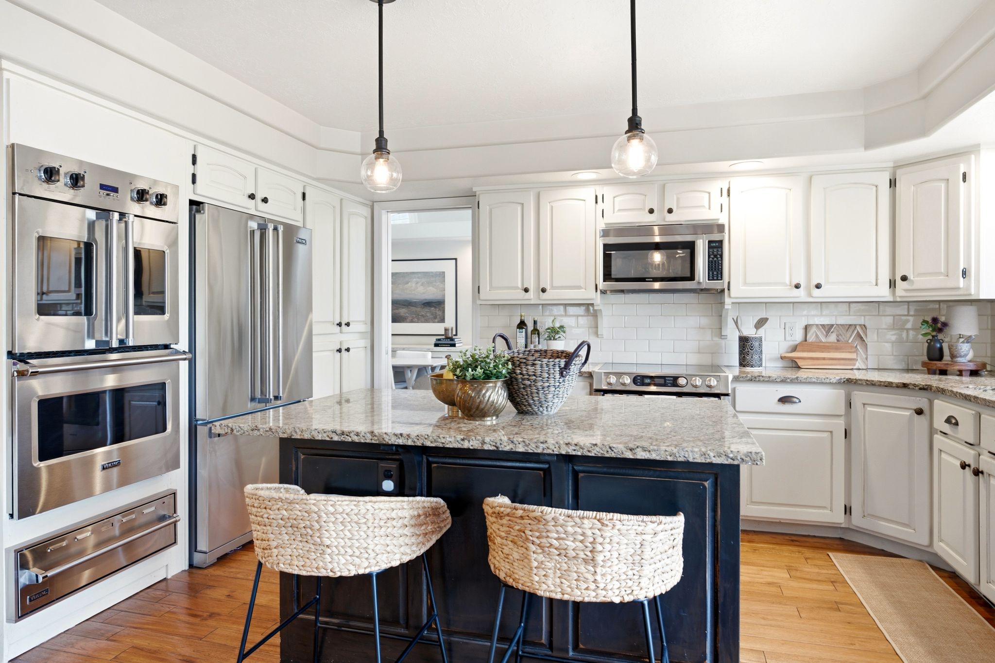 Kitchen featuring a large island with stone-finish countertop, stainless steel appliance suite, white subway tile backsplash, and wood-finish flooring