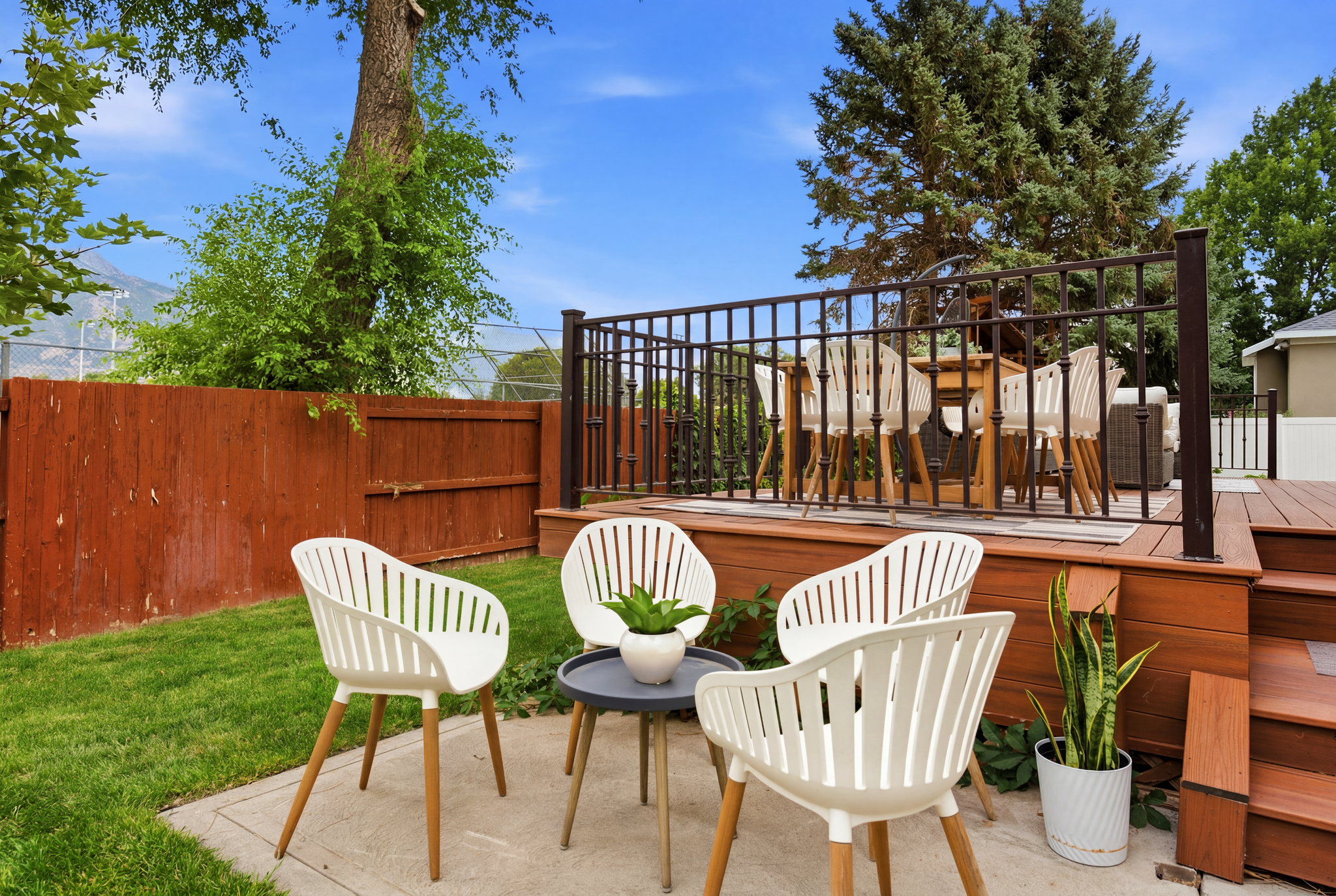 Multi-level wood-finish decking featuring a wrought-iron railing and steps down to a concrete patio area
