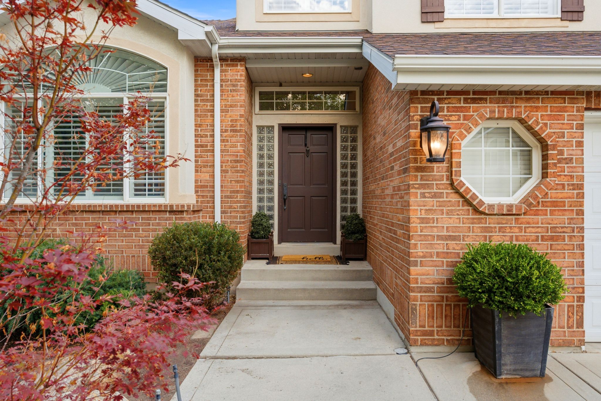 Brick facade residence featuring a dark paneled entry door, sidelight glass block windows, and an octagonal window with a decorative surround